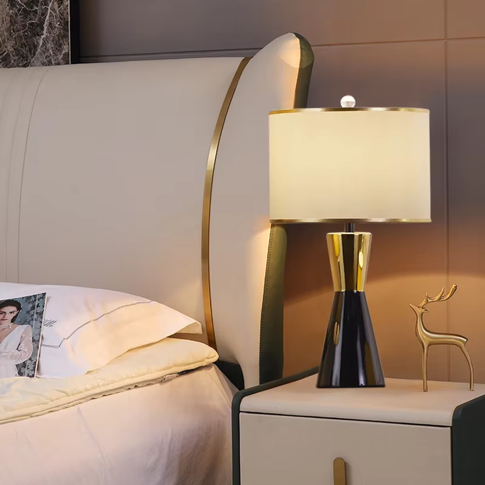 This is a light luxury black-gold cone table lamp, with a black cone base paired with golden decorations, a beige cylindrical lampshade with golden trim, soft and warm lighting, creating an elegant light luxury atmosphere.