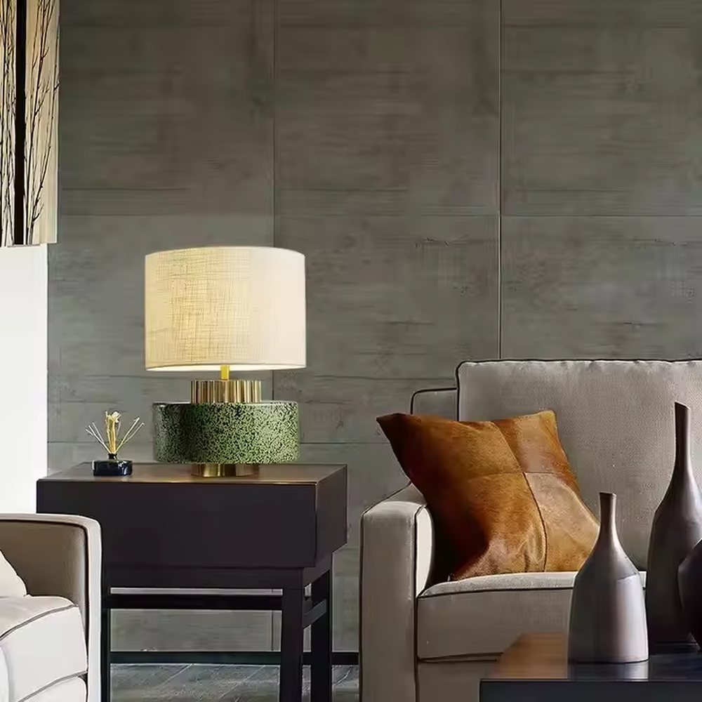 This is a modern artistic green and gold table lamp, with a green textured base, golden metal ring, and beige fabric circular lampshade, featuring a minimalist and grand design with both artistic sense and texture. It is used for local desktop lighting and decoration, creating a modern artistic atmosphere. It is suitable for modern minimalist home bedroom bedside tables, artistic-style living room side tables, high-end hotel guest rooms and other places.