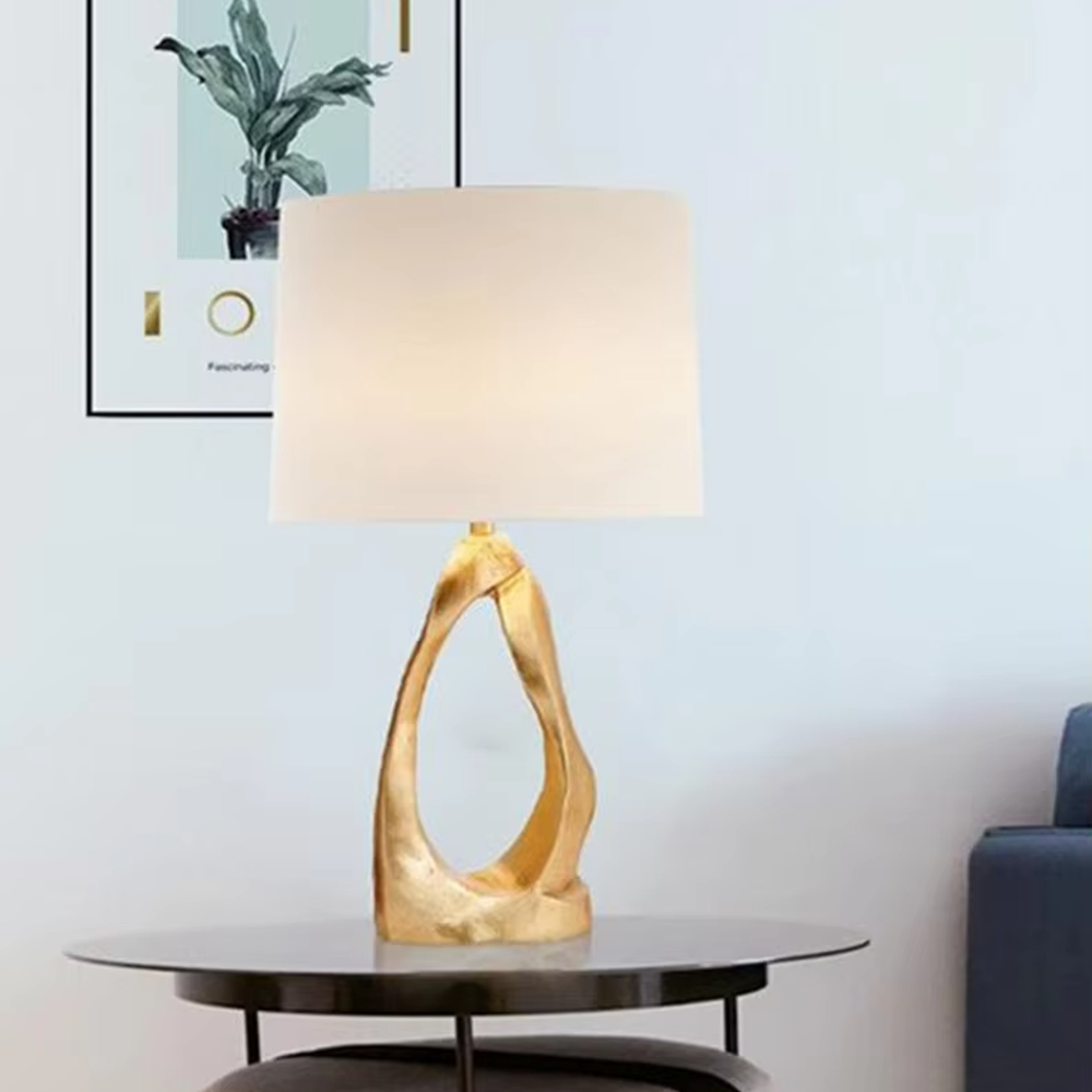 Art light luxury golden irregular twisted hollow base table lamp, beige fabric cylindrical lampshade, soft warm light, creating a high-end art light luxury atmosphere.