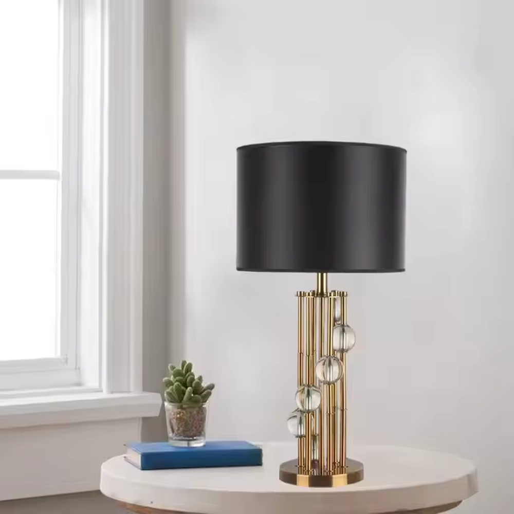 This is a luxury black-gold crystal table lamp, with a golden metal column (with multiple thin columns design) and transparent crystal balls, a black cylindrical fabric lampshade, featuring a modern luxury design with high-quality texture. It is used for local desktop lighting and decoration, creating a high-end luxury atmosphere. It is suitable for luxury-style home bedroom bedside tables, high-end hotel guest rooms, modern soft decoration display spaces and other places.