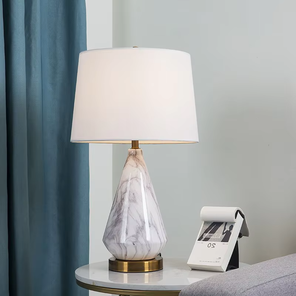 This is a light luxury marble-patterned cone table lamp, with a white fabric lampshade paired with a black-gray-white textured cone base, decorated with a golden metal base at the bottom and a small golden ball at the top. The lighting is soft and warm, creating an elegant light luxury atmosphere.
