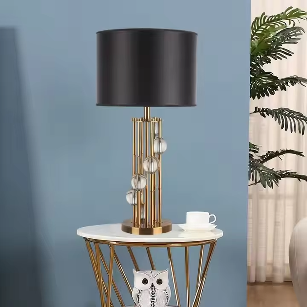 This is a luxury black-gold crystal table lamp, with a golden metal column (with multiple thin columns design) and transparent crystal balls, a black cylindrical fabric lampshade, featuring a modern luxury design with high-quality texture. It is used for local desktop lighting and decoration, creating a high-end luxury atmosphere. It is suitable for luxury-style home bedroom bedside tables, high-end hotel guest rooms, modern soft decoration display spaces and other places.