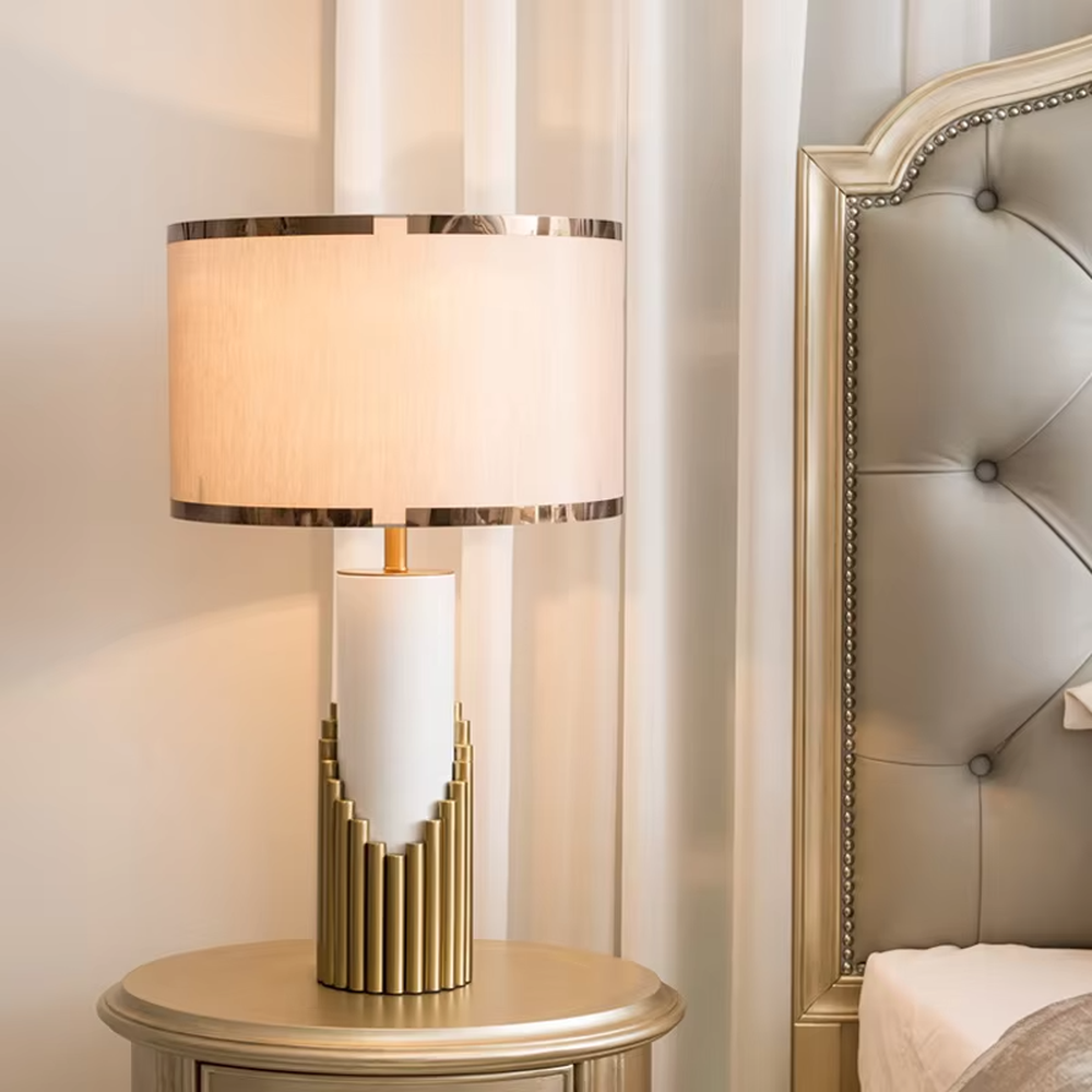 This is a light luxury-style gold and white metal fabric table lamp, with a golden staggered metal column base, paired with a white cylinder and a beige fabric lampshade (golden edging). It features a minimalist light luxury design, with warm and soft lighting. It is used for local desktop lighting and decoration, creating a light luxury and warm atmosphere. Suitable for light luxury-style bedroom bedside tables, modern minimalist living room side tables, high-end hotel guest rooms and other places.