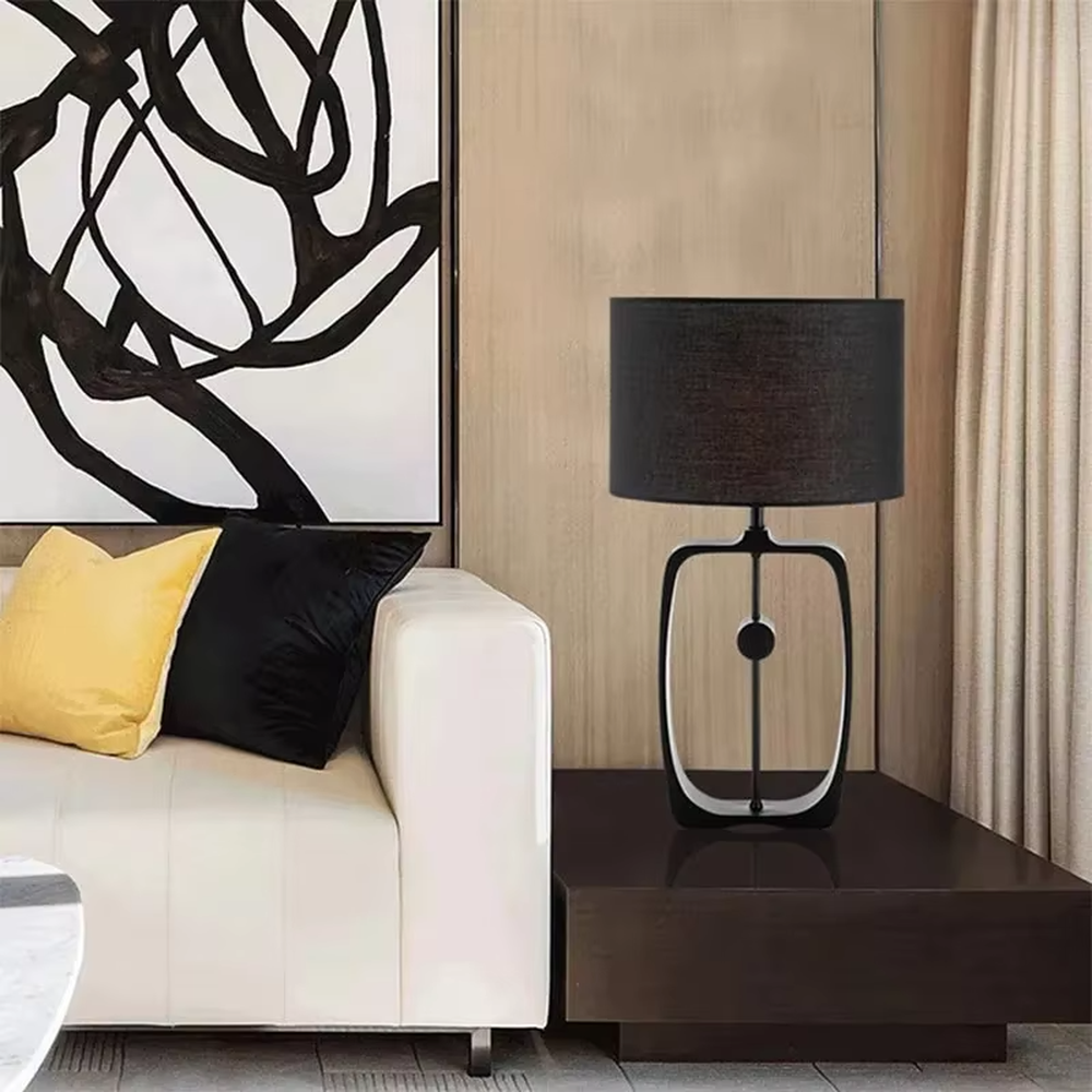Modern minimalist black hollow frame table lamp, black fabric cylindrical lampshade + metal hollow rectangular base, soft and high-end lighting, creating a minimalist textured atmosphere.