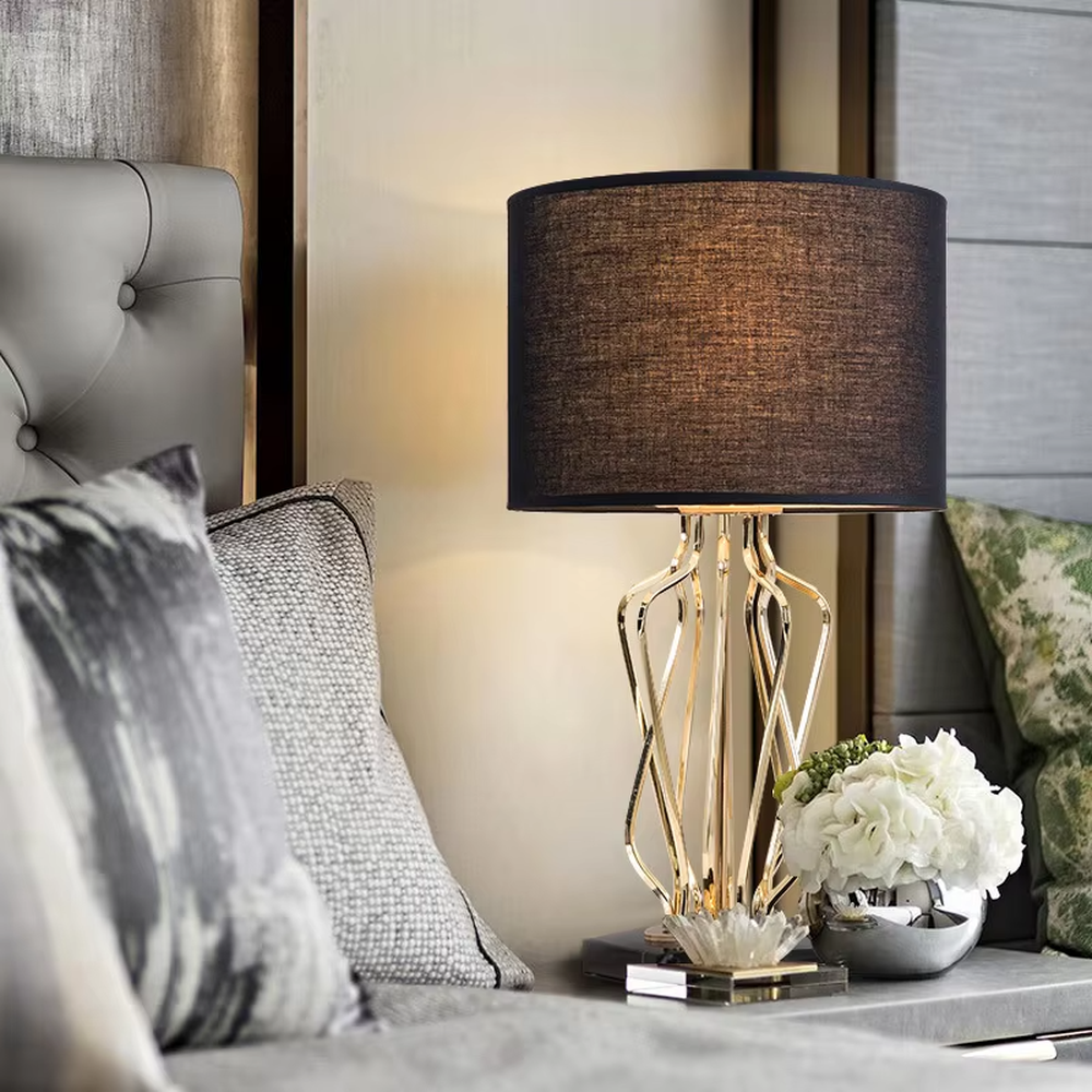 Light luxury golden interlaced hollow table lamp, white cylindrical fabric lampshade + black base, soft and warm lighting, creating a high-end elegant atmosphere.