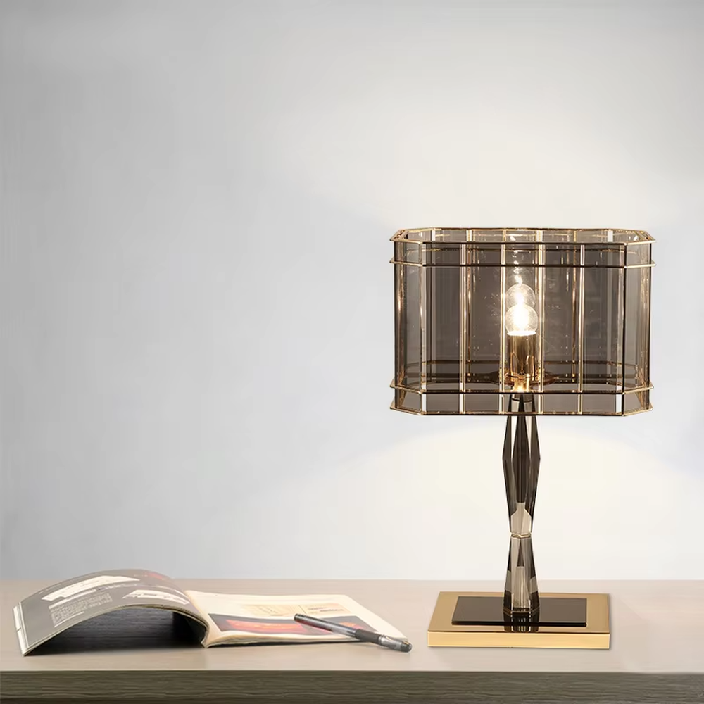 This is a light luxury and luxurious smoky gray glass metal table lamp, with a smoky gray glass lampshade paired with a golden metal frame, a golden base, and a geometrically cut lamp post. It features an exquisite and grand design, with soft and textured lighting through the glass. It is used for local desktop lighting and decoration, creating a light luxury and luxurious atmosphere. Suitable for light luxury-style bedroom bedside tables, luxury living room side tables, high-end hotel guest rooms and other places.