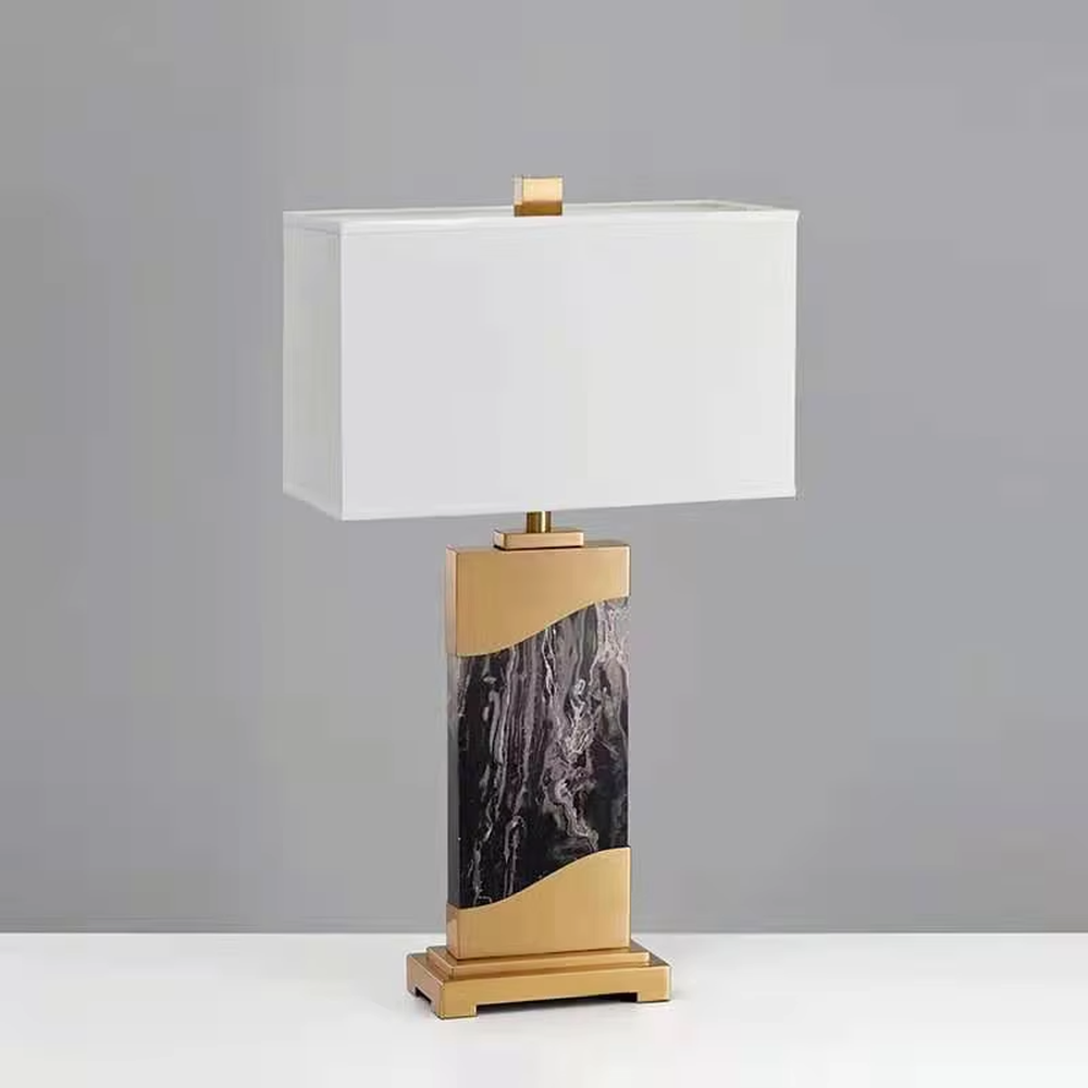 This is a luxury black-gold marble table lamp, with a golden metal frame, black-veined marble (with curved design), and a white fabric square lampshade, featuring a minimalist luxury design with high-quality texture. It is used for local desktop lighting and decoration, creating a high-end luxury atmosphere. It is suitable for luxury-style home bedroom bedside tables, high-end hotel guest rooms, modern soft decoration display spaces and other places.