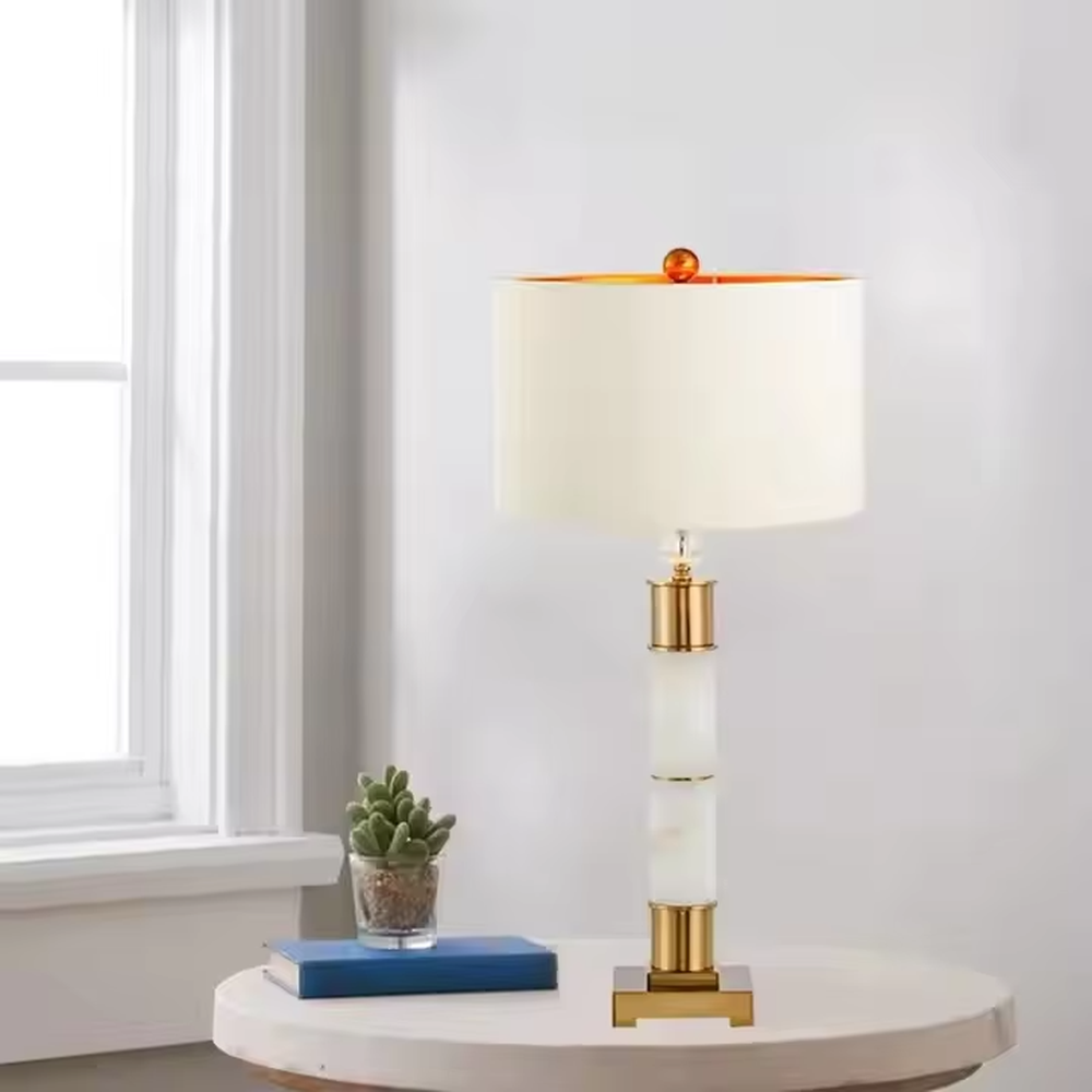 This is a luxury-style gold and white table lamp, combining golden metal and white cylinder, with a beige fabric circular lampshade, featuring a minimalist and grand design with strong luxury texture. It is used for local desktop lighting and decoration, creating a luxury and warm atmosphere. It is suitable for luxury-style home bedroom bedside tables, high-end hotel guest rooms, modern minimalist living room side tables and other places.