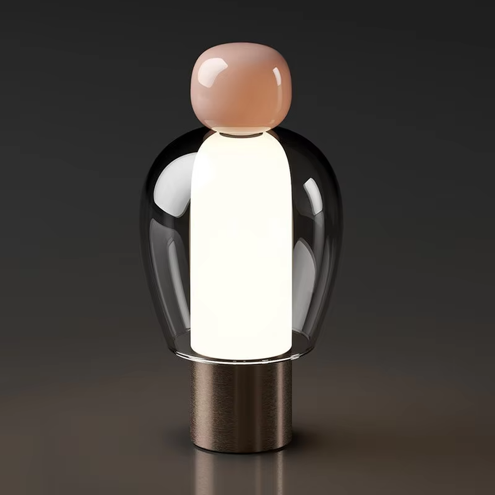 This is an artistic doll-style glass and metal table lamp, with a transparent glass shell, pink top, and metal base. Its unique shape is like an artistic doll, featuring a strong modern artistic sense. It is used for local desktop lighting and decoration, creating an artistic and modern atmosphere. Suitable for art exhibition halls, corners of modern home studies, designer studios and other places.