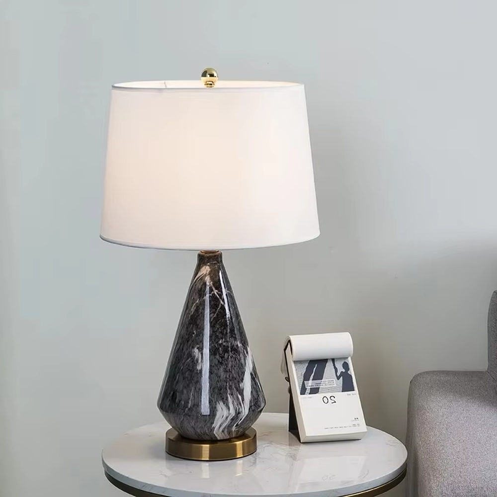 This is a light luxury marble-patterned cone table lamp, with a white fabric lampshade paired with a black-gray-white textured cone base, decorated with a golden metal base at the bottom and a small golden ball at the top. The lighting is soft and warm, creating an elegant light luxury atmosphere.