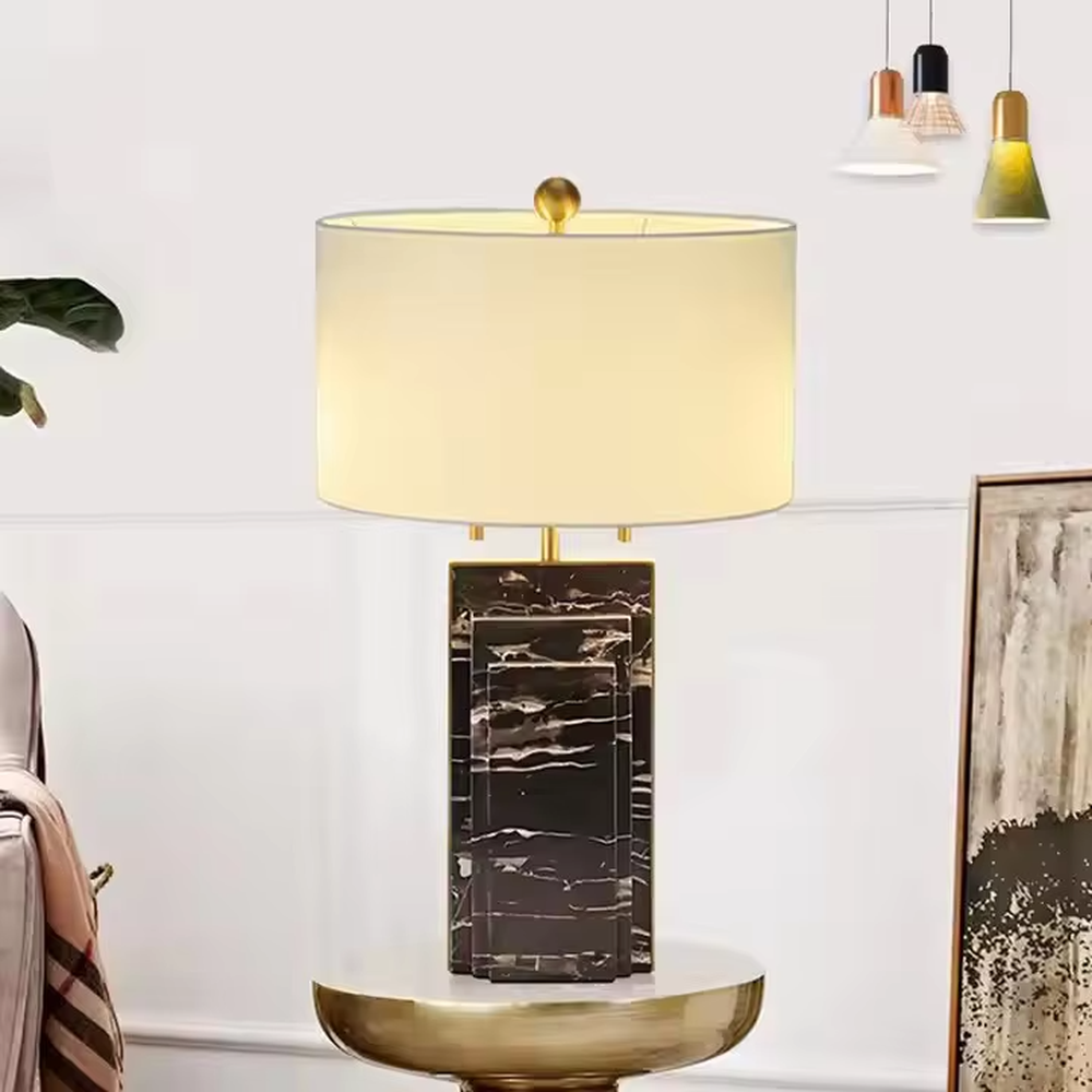 This is a luxury-style black-gold marble table lamp, with a black marble-textured base, golden metal parts, and a beige fabric circular lampshade, featuring a minimalist and grand design with strong luxury texture. It is used for local desktop lighting and decoration, creating a luxury and modern atmosphere. It is suitable for luxury-style home bedroom bedside tables, high-end hotel guest rooms, modern minimalist living room side tables and other places.