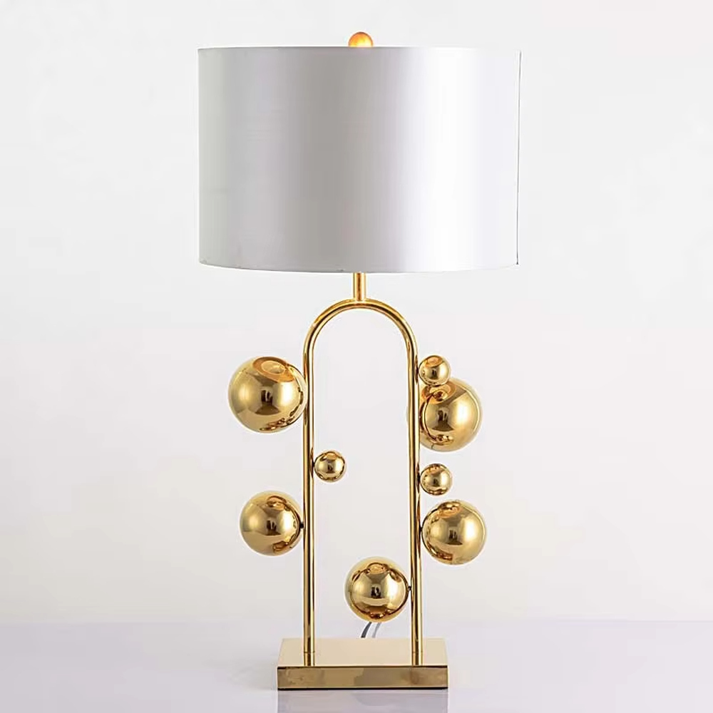 This is a light luxury modern-style golden ball table lamp, with a golden metal frame paired with multi-sized golden ball decorations, a black cylindrical lampshade + a golden square base, featuring a high-end and exquisite style, with soft and stylish lighting.
