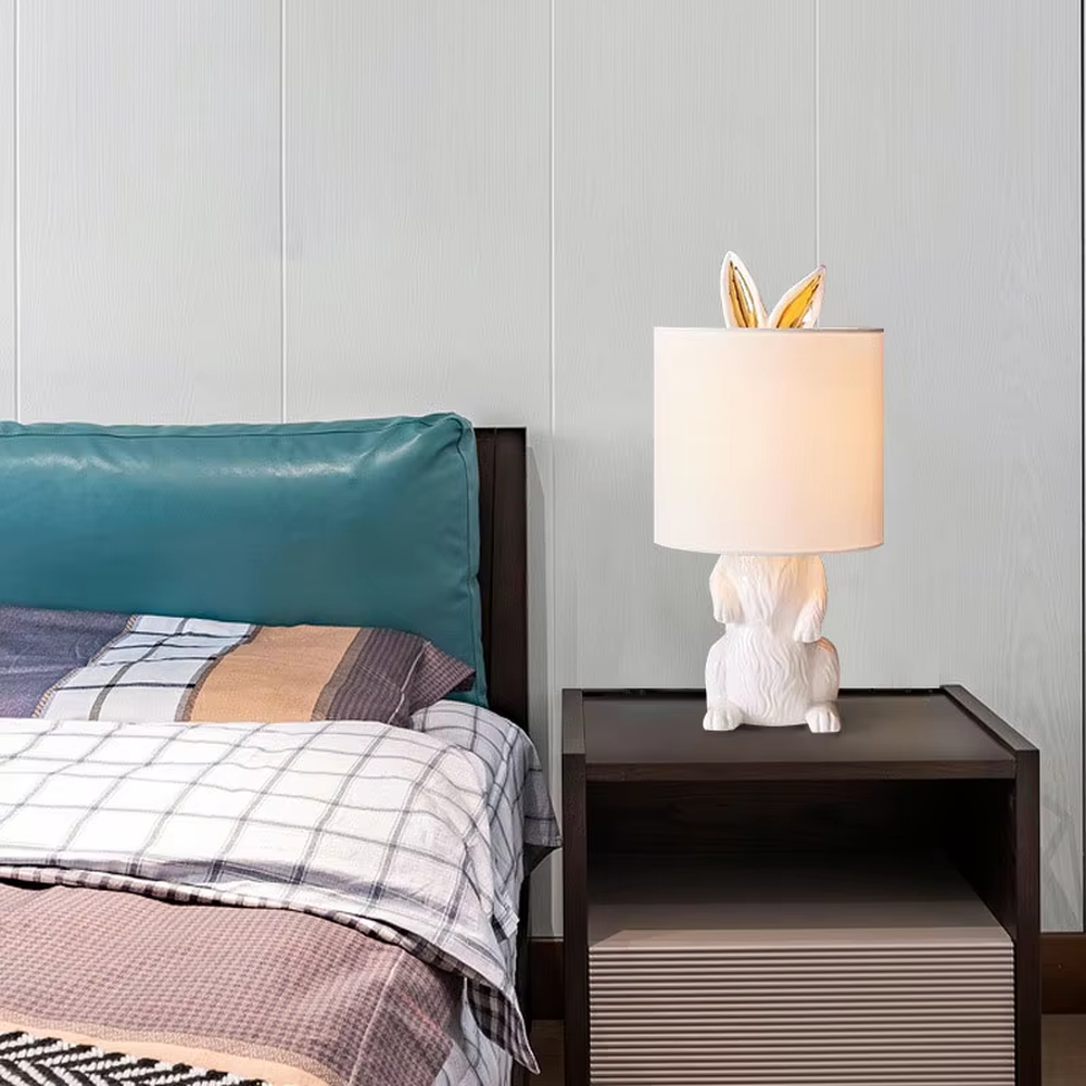 This is a cute and adorable rabbit-shaped table lamp, with a white rabbit-shaped base paired with golden ear decorations, and a white cylindrical lampshade. It has a warm and cute style, with soft and comfortable lighting.