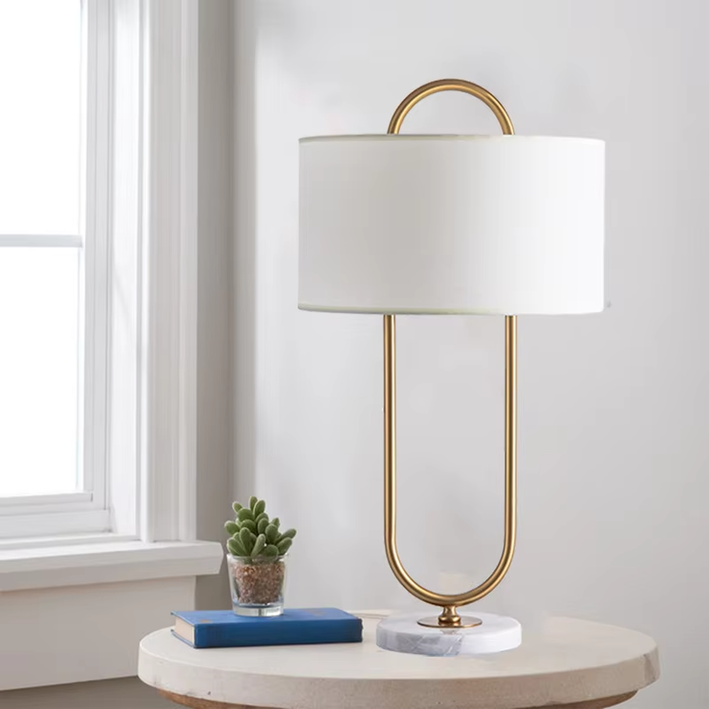 Light luxury golden geometric line base table lamp, beige fabric gold-edged lampshade + golden U-shaped multi-layer frame + white small ball decoration, soft warm light, creating a modern light luxury atmosphere.