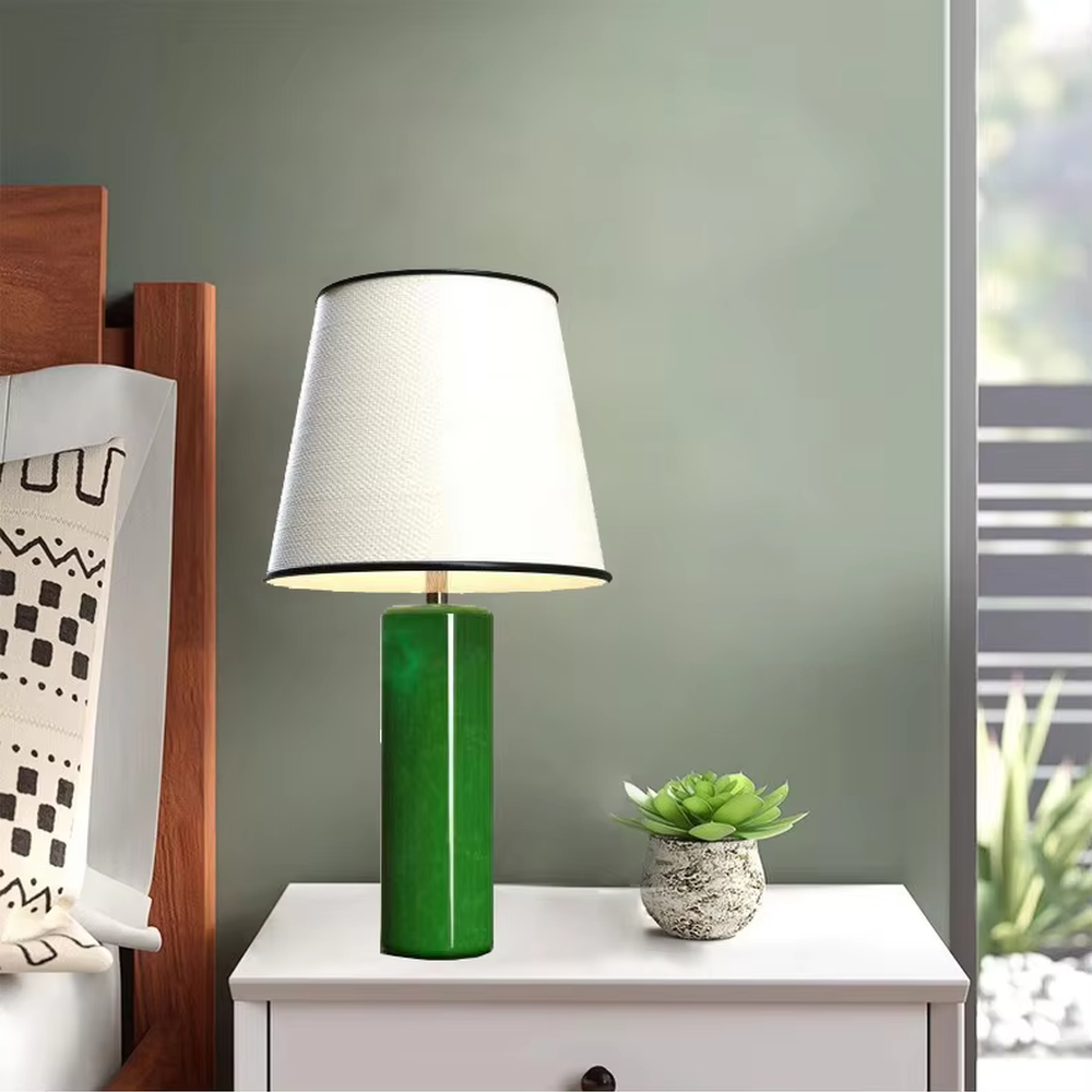 This is a modern fresh-style green cylindrical table lamp, with a green cylindrical base and a white fabric lampshade (black edging), featuring a minimalist modern design and fresh style. It is used for local desktop lighting and decoration, creating a fresh and modern atmosphere. Suitable for modern minimalist bedroom bedside tables, Nordic-style living room side tables, creative studios and other places.