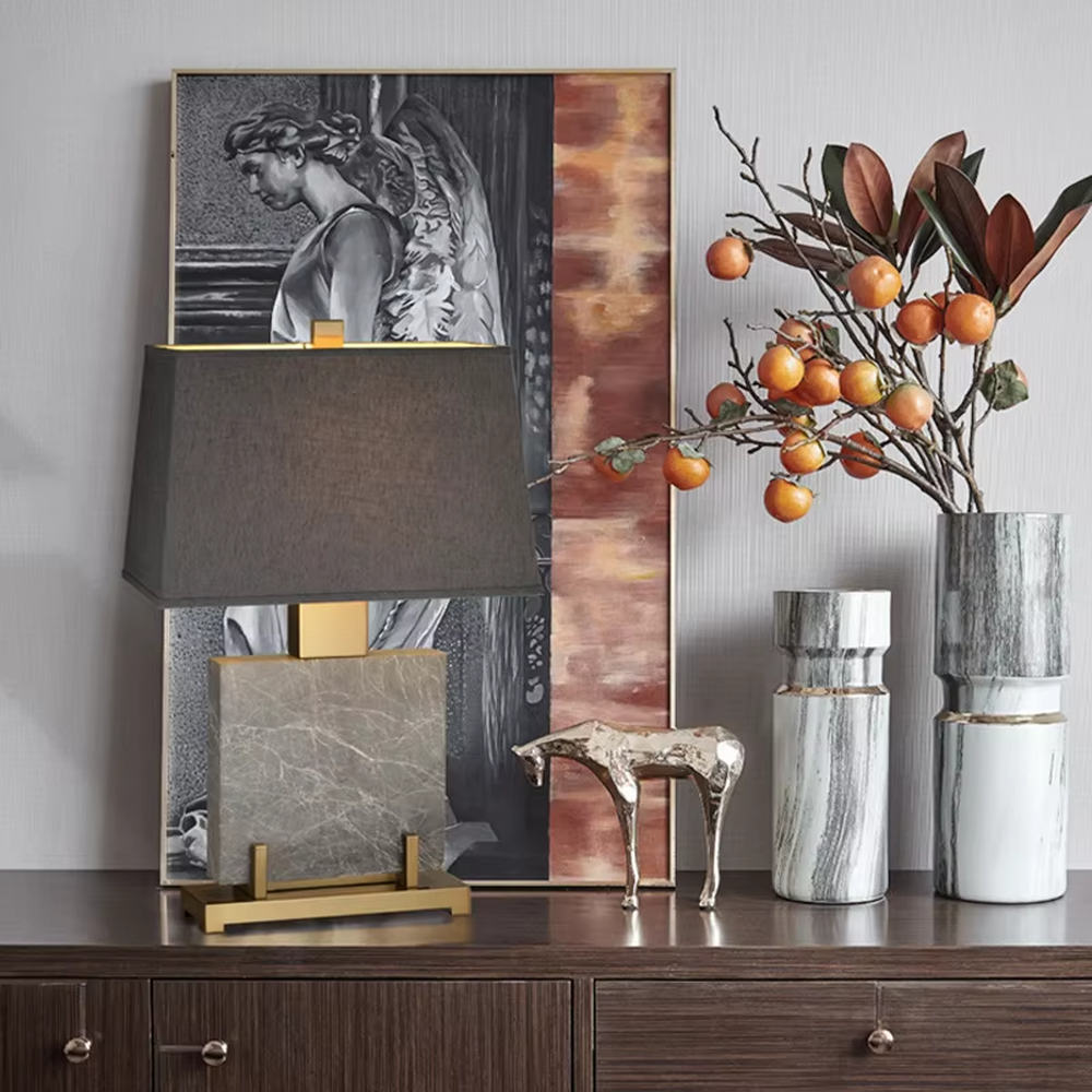 This is a light luxury modern-style marble metal fabric table lamp, with a gray marble base paired with golden metal brackets and connectors, and a gray fabric square lampshade. It features a minimalist and grand design with high texture. It is used for local desktop lighting and decoration, creating a light luxury and elegant atmosphere. Suitable for light luxury-style bedroom bedside tables, modern minimalist living room side tables, high-end hotel guest rooms and other places.