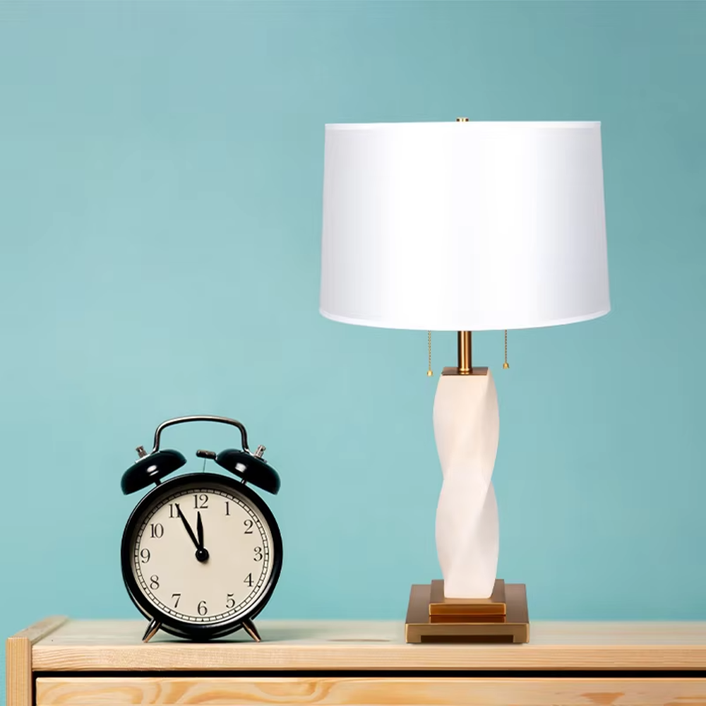 This is a modern artistic twisted table lamp, with a white twisted base, golden metal components, and a white fabric circular lampshade, featuring a strong artistic sense and luxury texture. It is used for local desktop lighting and decoration, creating an artistic luxury atmosphere. It is suitable for modern art home bedroom bedside tables, designer studios, high-end hotel guest rooms and other places.