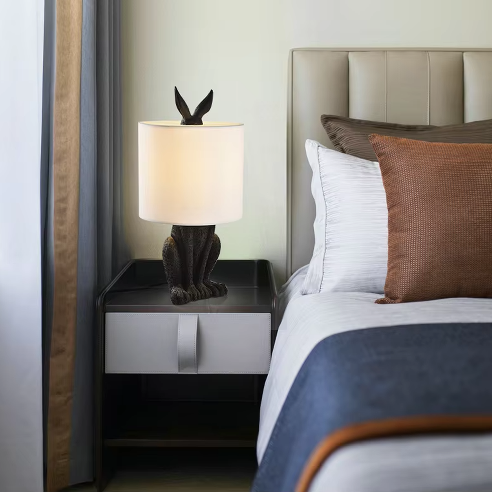 This is a cute and adorable rabbit-shaped table lamp, with a white rabbit-shaped base paired with golden ear decorations, and a white cylindrical lampshade. It has a warm and cute style, with soft and comfortable lighting.