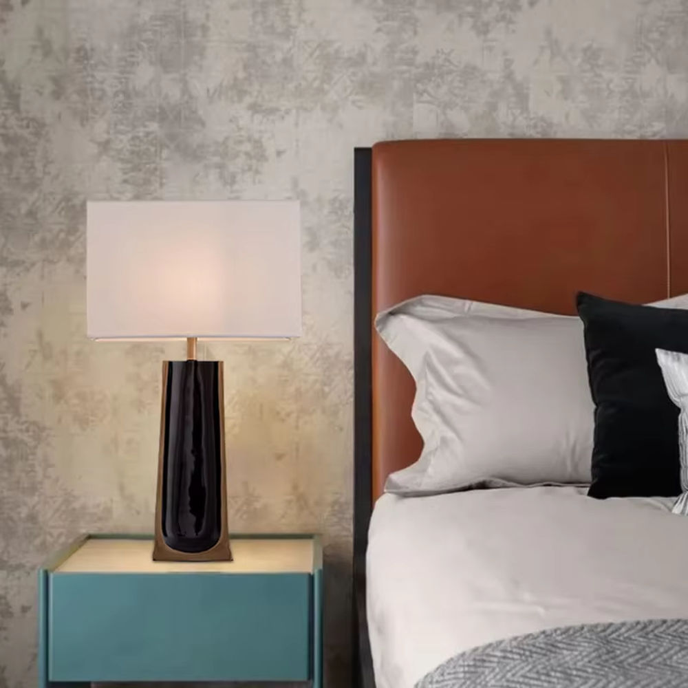 This is a light luxury modern-style black and gold column fabric table lamp, with a black and gold column base (with golden decorative edges) paired with a white fabric square lampshade. It features a minimalist light luxury design, with warm and soft lighting. It is used for local desktop lighting and decoration, creating a light luxury elegant atmosphere. Suitable for light luxury-style bedroom bedside tables, modern minimalist living room side tables, high-end hotel guest rooms and other places.