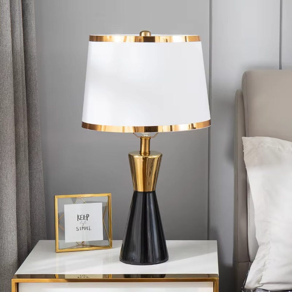 This is a light luxury black-gold cone table lamp, with a black cone base paired with golden decorations, a beige cylindrical lampshade with golden trim, soft and warm lighting, creating an elegant light luxury atmosphere.