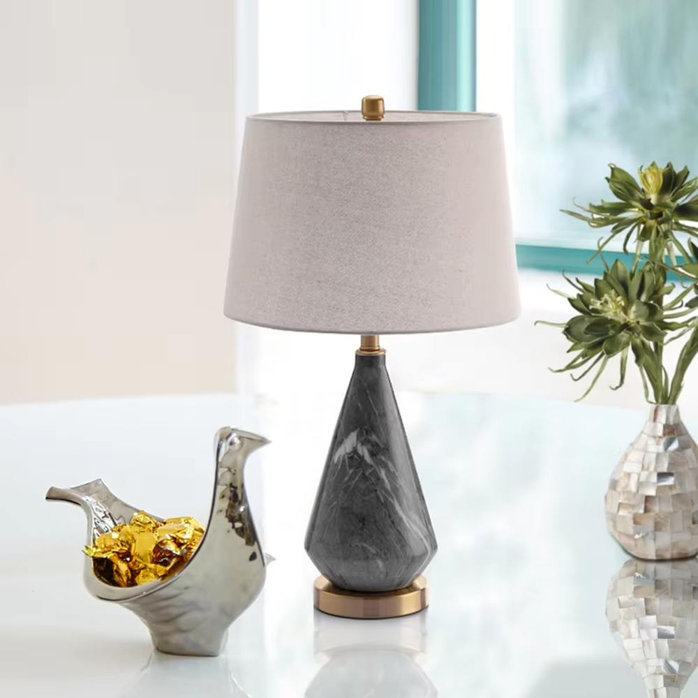 This is a light luxury marble-patterned cone table lamp, with a white fabric lampshade paired with a black-gray-white textured cone base, decorated with a golden metal base at the bottom and a small golden ball at the top. The lighting is soft and warm, creating an elegant light luxury atmosphere.