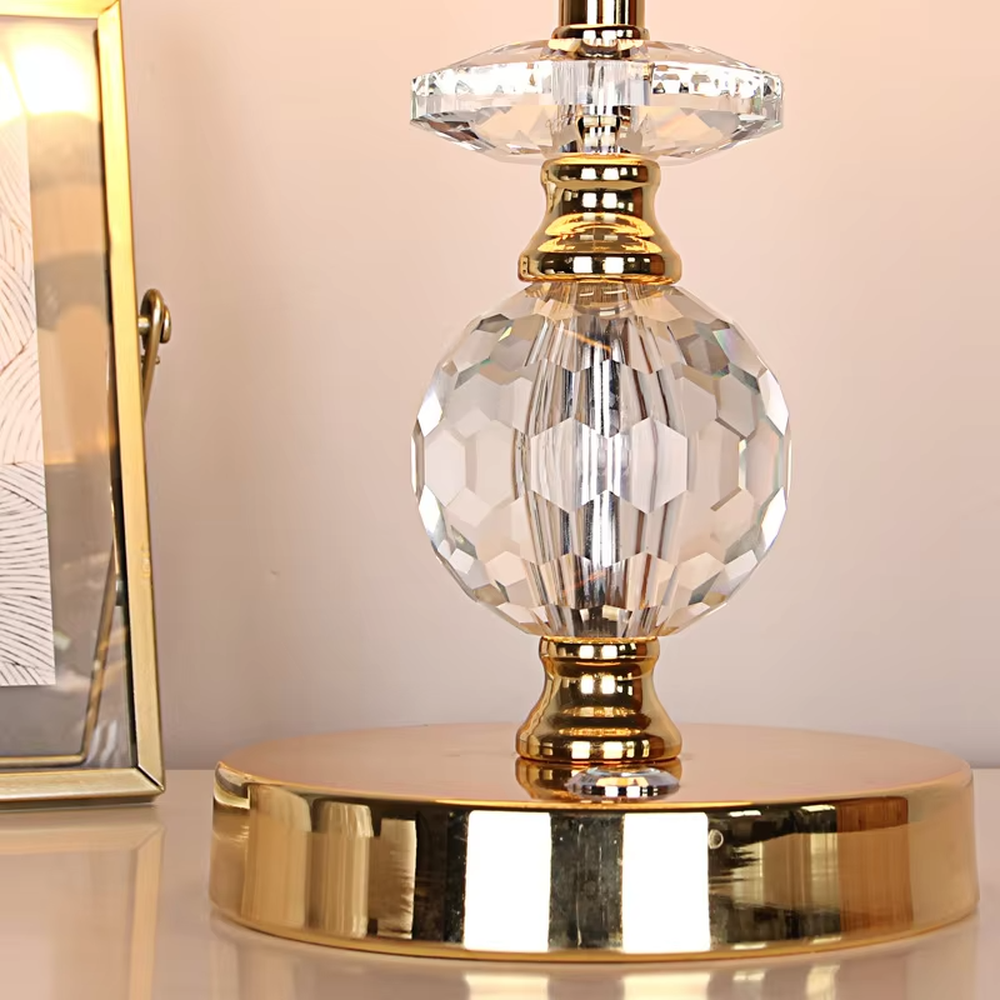 This is a light luxury exquisite fabric crystal table lamp, with a beige fabric lampshade paired with a golden trim, a golden metal lamp pole embedded with transparent cut crystal decorations, a high-quality golden base, and soft and elegant lighting, creating a light luxury exquisite atmosphere.