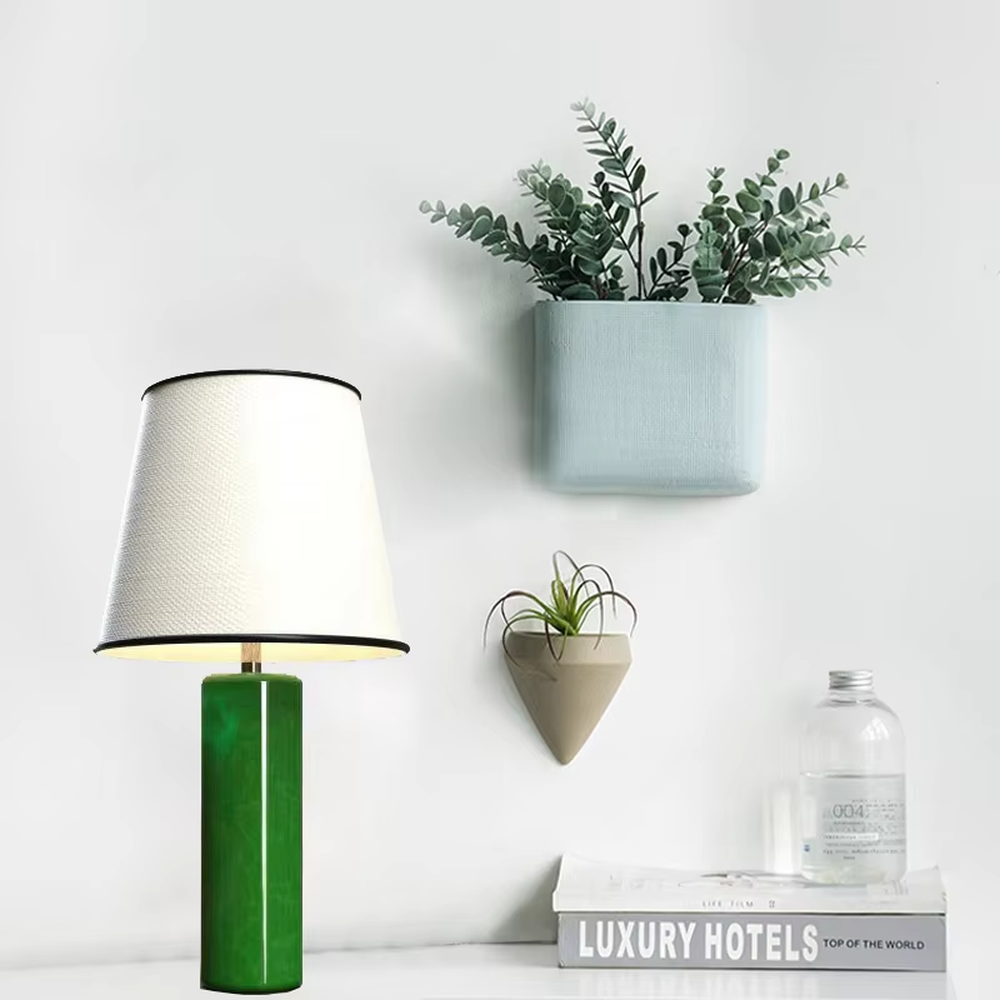 This is a modern fresh-style green cylindrical table lamp, with a green cylindrical base and a white fabric lampshade (black edging), featuring a minimalist modern design and fresh style. It is used for local desktop lighting and decoration, creating a fresh and modern atmosphere. Suitable for modern minimalist bedroom bedside tables, Nordic-style living room side tables, creative studios and other places.