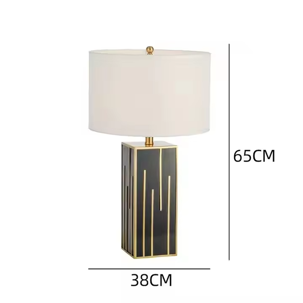 This is a luxury geometric - shaped table lamp with a black - gold geometric base (decorated with gold lines) and a white cylindrical fabric lampshade, featuring a minimalist luxury design with strong modern artistic sense. It is used for local desktop lighting and decoration, creating a luxurious and elegant atmosphere. It is suitable for luxury - style home bedroom bedside tables, high - end hotel guest rooms, modern soft decoration display spaces and other places.