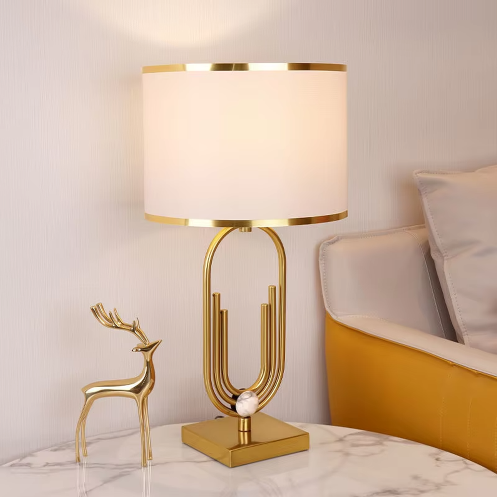 This is a light luxury artistic golden oval metal table lamp, with a golden metal oval frame with line decorations, paired with a beige fabric round lampshade. It features a light luxury and elegant design, with warm and soft lighting. It is used for local desktop lighting and decoration, creating a light luxury artistic atmosphere. Suitable for light luxury-style bedroom bedside tables, modern minimalist living room side tables, high-end hotel guest rooms and other places.