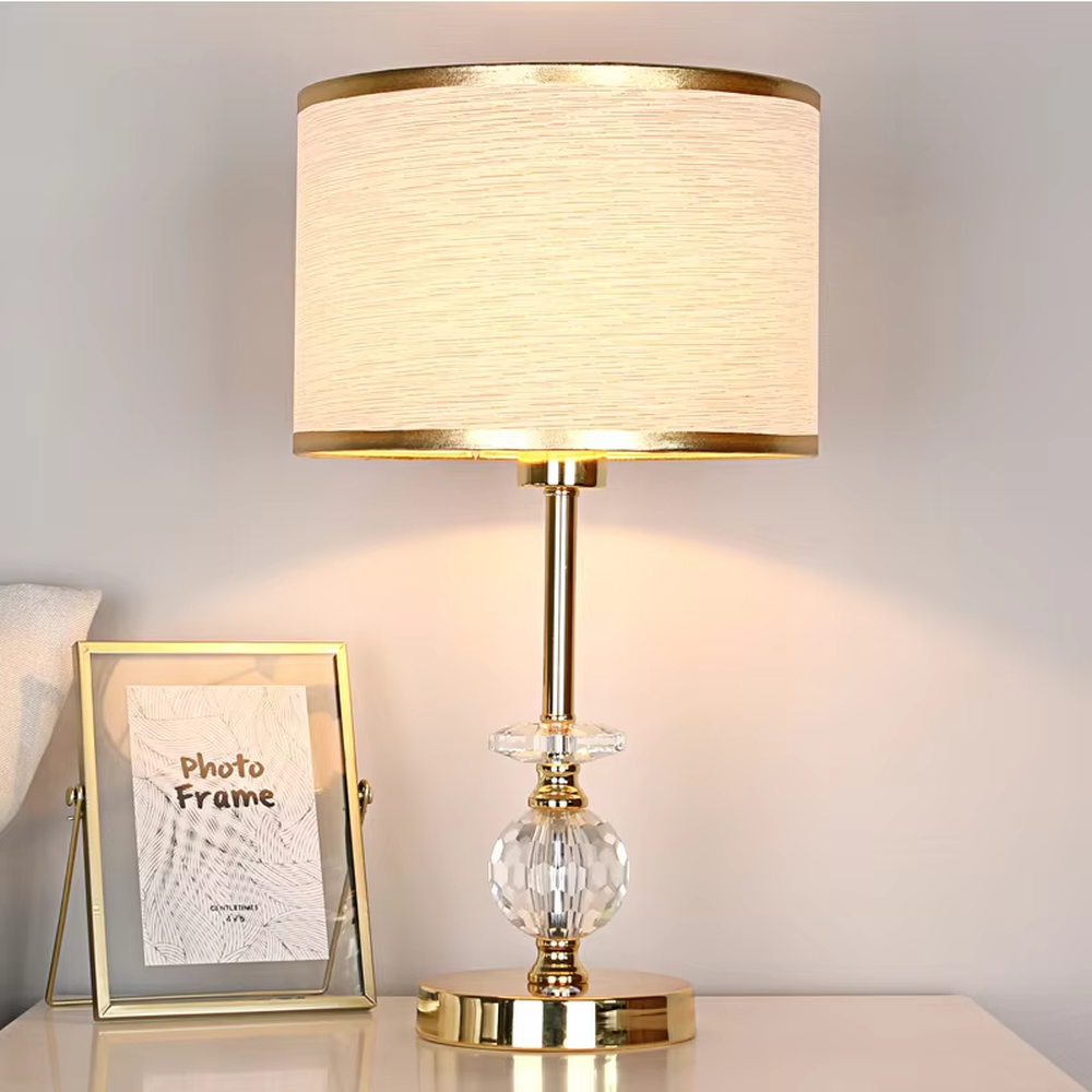 This is a light luxury exquisite fabric crystal table lamp, with a beige fabric lampshade paired with a golden trim, a golden metal lamp pole embedded with transparent cut crystal decorations, a high-quality golden base, and soft and elegant lighting, creating a light luxury exquisite atmosphere.