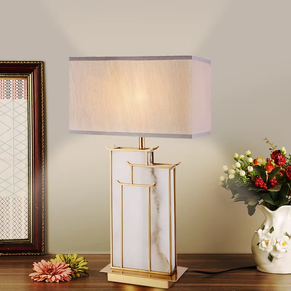New Chinese light luxury gold frame ink texture table lamp, gold window lattice-like metal frame + ink texture panel + beige fabric lampshade, soft lighting, creating an elegant new Chinese atmosphere.