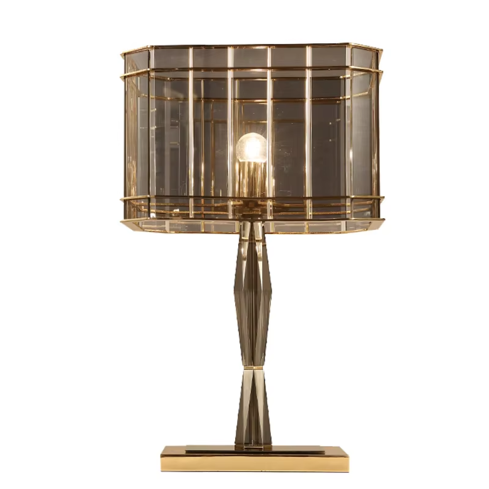 This is a light luxury and luxurious smoky gray glass metal table lamp, with a smoky gray glass lampshade paired with a golden metal frame, a golden base, and a geometrically cut lamp post. It features an exquisite and grand design, with soft and textured lighting through the glass. It is used for local desktop lighting and decoration, creating a light luxury and luxurious atmosphere. Suitable for light luxury-style bedroom bedside tables, luxury living room side tables, high-end hotel guest rooms and other places.