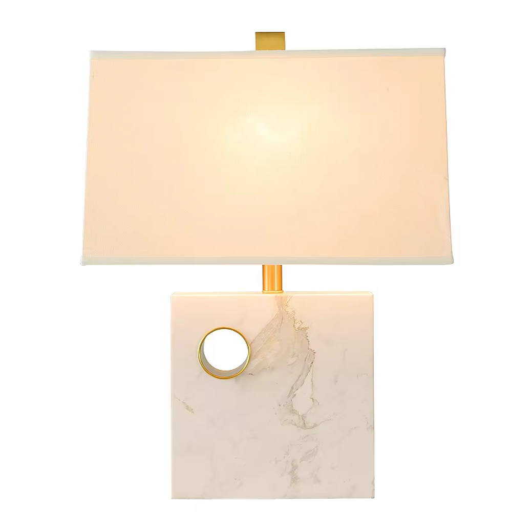 This is a light luxury elegant marble-based fabric table lamp, with a white marble base with golden ring decoration, paired with a beige fabric square lampshade and golden metal connectors. It features a minimalist light luxury design, with warm and soft lighting. It is used for local desktop lighting and decoration, creating a light luxury elegant atmosphere. Suitable for light luxury-style bedroom bedside tables, modern minimalist studies, high-end hotel guest rooms and other places.