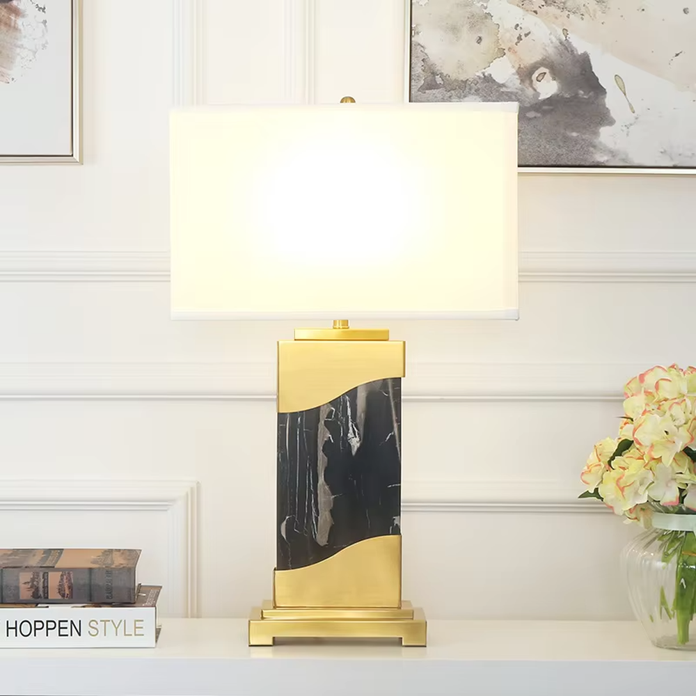 This is a luxury black-gold marble table lamp, with a golden metal frame, black-veined marble (with curved design), and a white fabric square lampshade, featuring a minimalist luxury design with high-quality texture. It is used for local desktop lighting and decoration, creating a high-end luxury atmosphere. It is suitable for luxury-style home bedroom bedside tables, high-end hotel guest rooms, modern soft decoration display spaces and other places.