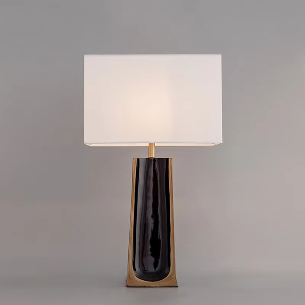 This is a light luxury modern-style black and gold column fabric table lamp, with a black and gold column base (with golden decorative edges) paired with a white fabric square lampshade. It features a minimalist light luxury design, with warm and soft lighting. It is used for local desktop lighting and decoration, creating a light luxury elegant atmosphere. Suitable for light luxury-style bedroom bedside tables, modern minimalist living room side tables, high-end hotel guest rooms and other places.