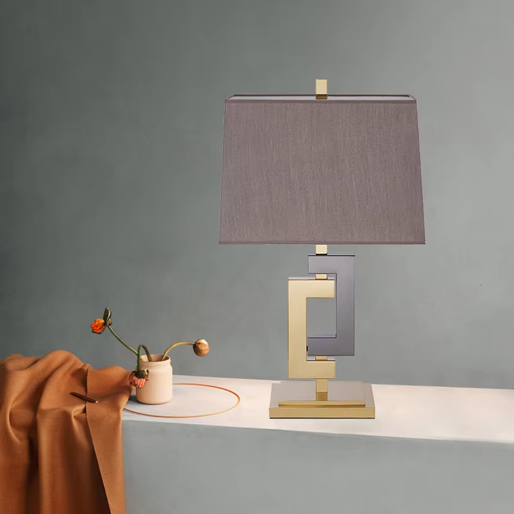 Light luxury gold-gray color-blocking geometric square frame table lamp, gold + dark gray metal geometric stand + dark gray fabric rectangular lampshade, soft and high-end lighting, creating a light luxury modern atmosphere.