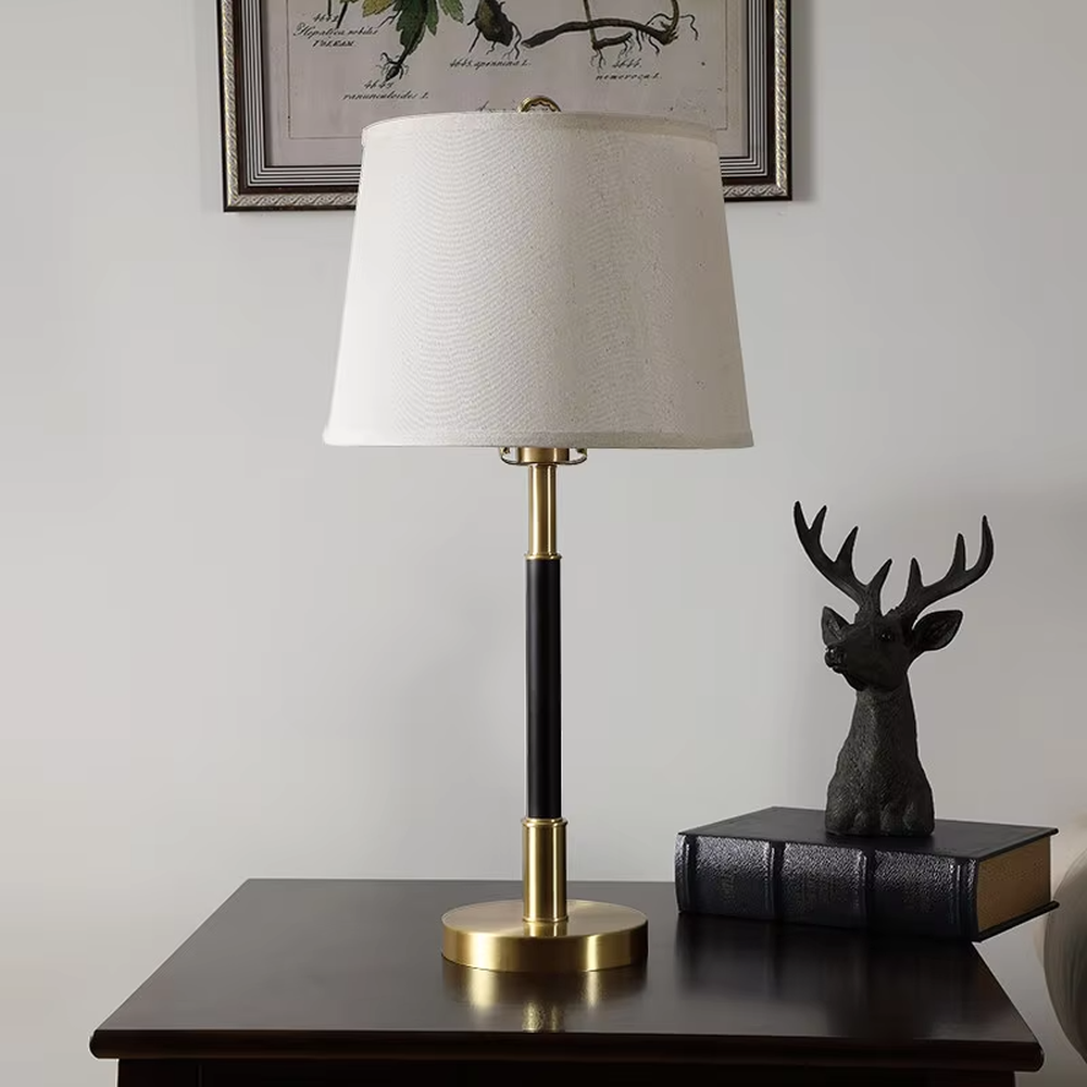 This table lamp features a black and gold contrasting metal lamp pole paired with an off-white fabric lampshade, with a glossy gold metal base. It presents a style that combines modern light luxury and minimalist retro, with soft eye-protective light, serving both lighting and decorative purposes, suitable for placement in bedrooms, studies and other spaces.