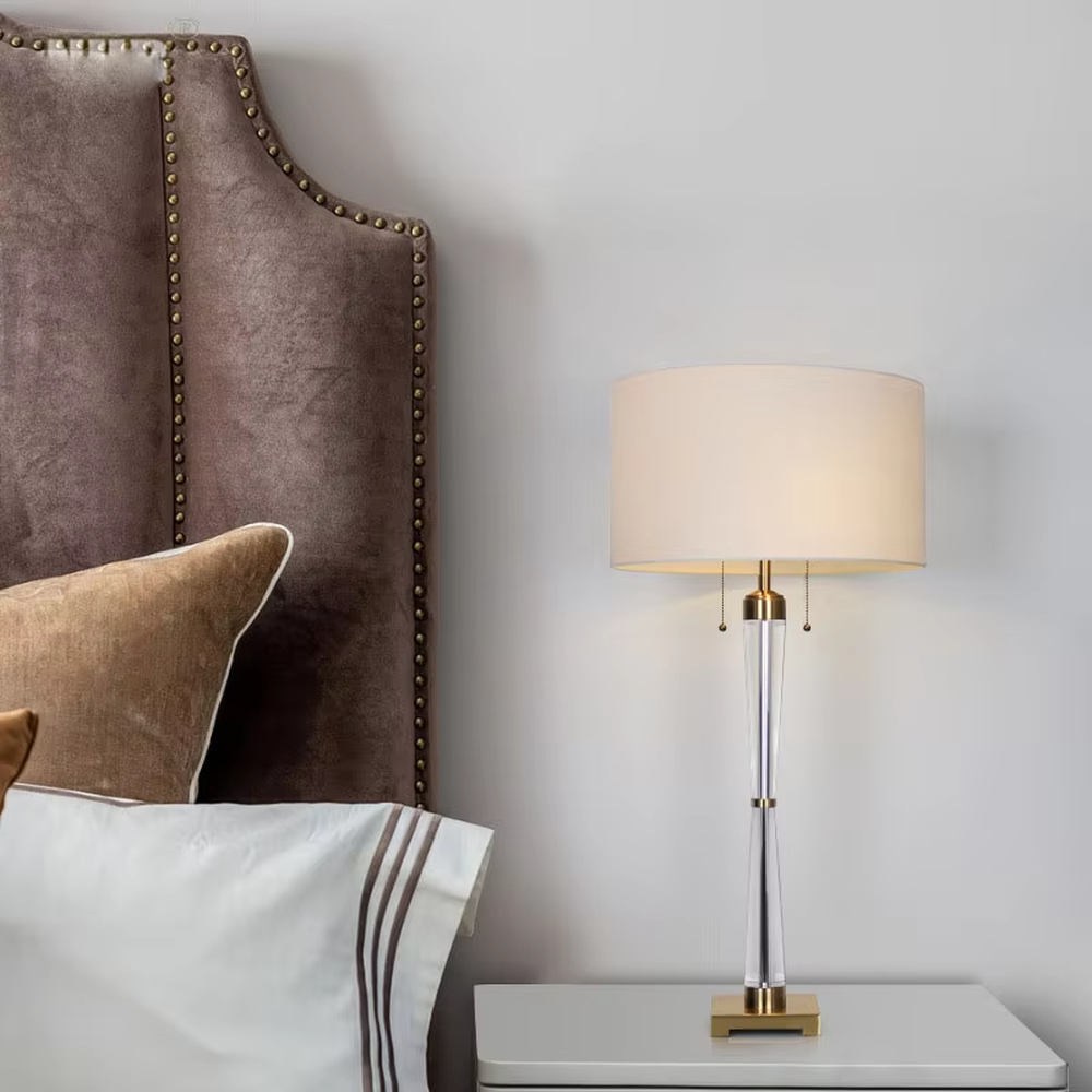 Modern light luxury fabric table lamp, with an off-white fabric lampshade paired with a transparent acrylic + gold metal spliced conical lamp pole, a gold square base with a double pull-cord switch, emitting soft and warm light, combining decorativeness and practicality, suitable for lighting and decoration in spaces such as bedroom nightstands, living room side tables, and hotel guest rooms.