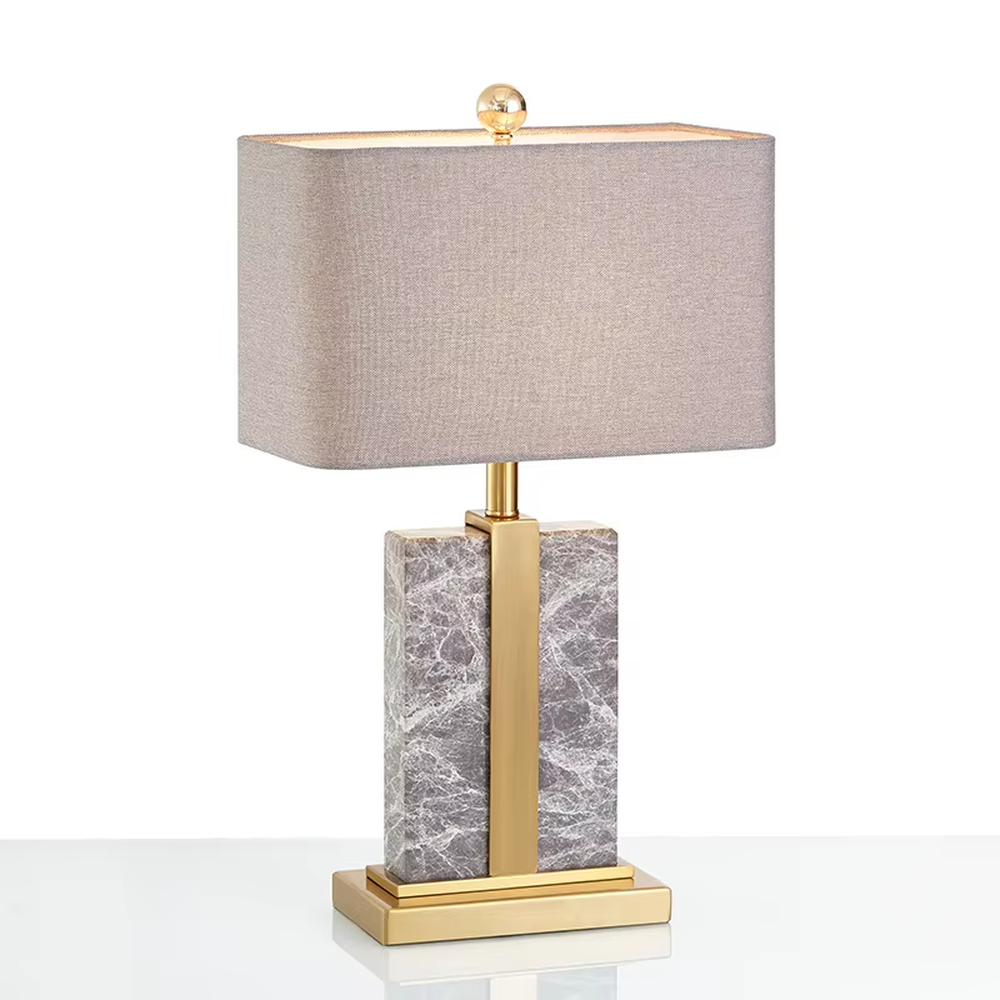 Modern light luxury marble and metal spliced table lamp, with a gray marble lamp body paired with gold metal decorative strips, a light gray fabric rectangular lampshade (with a gold ball decoration on top), emitting soft and elegant light, combining decorativeness and practicality, suitable for lighting and decoration in spaces such as bedroom nightstands, living room side tables, and hotel guest rooms.