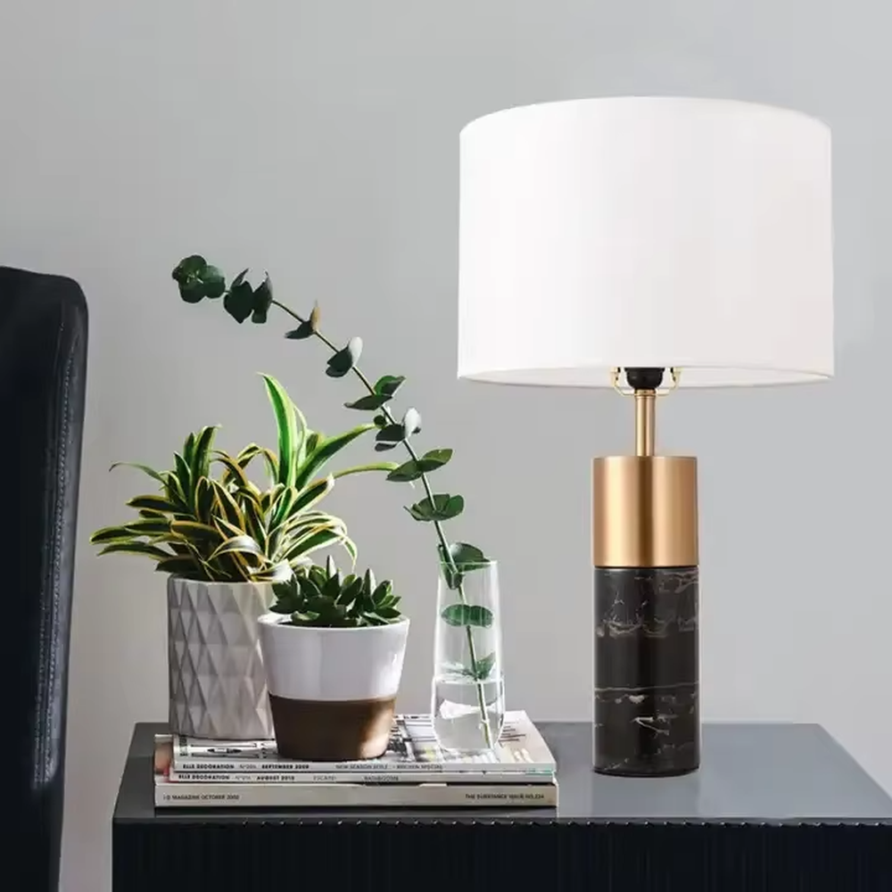 This light luxury modern table lamp features a lamp post made of black marble and gold metal, paired with an off-white fabric cylindrical lampshade. It has a calm and elegant shape, serves both lighting and decorative purposes, and is ideal for bedroom bedside tables, living room side tables, hotel guest rooms and light luxury commercial spaces.