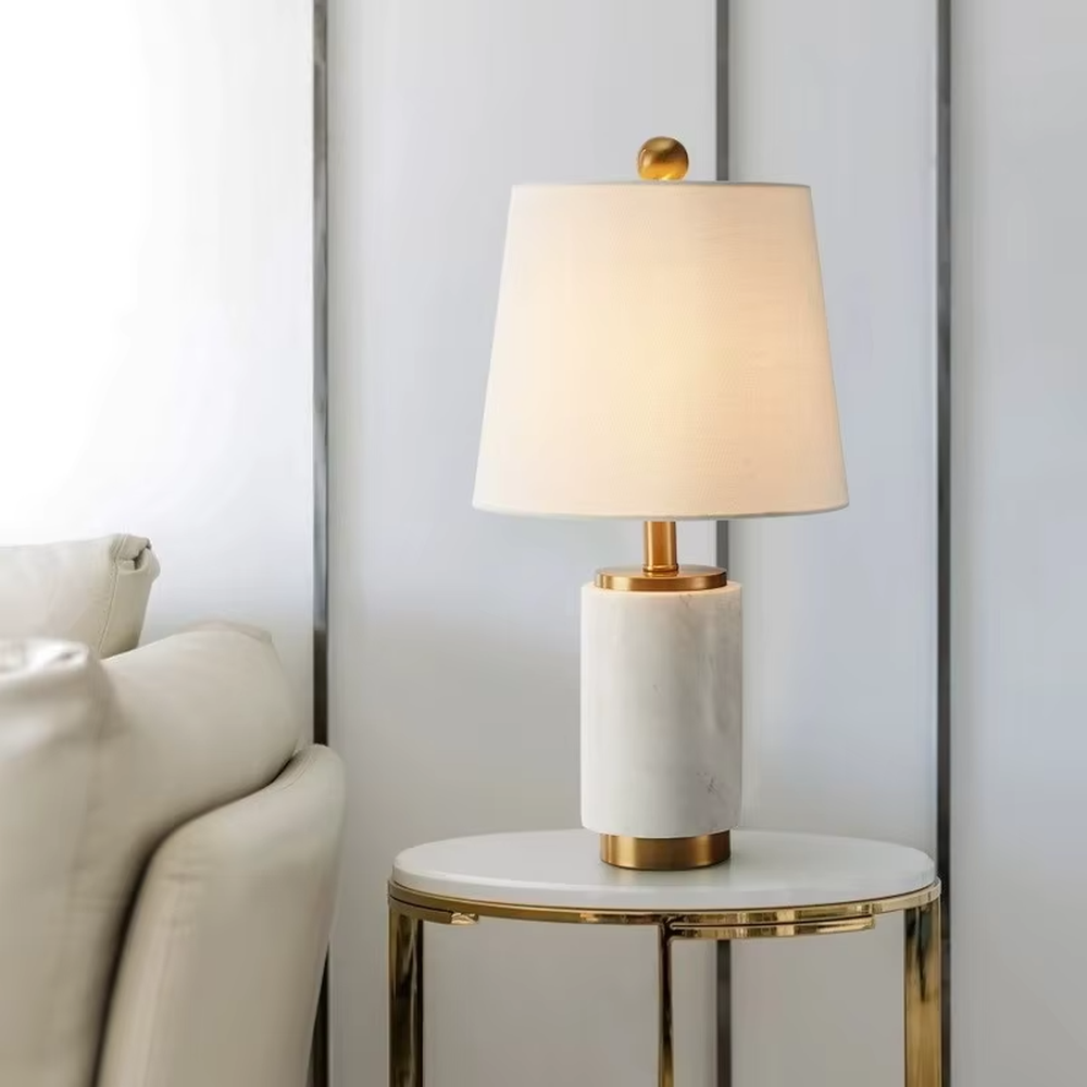 Light luxury white marble cylindrical table lamp, white marble base + golden metal decorations + beige fabric lampshade, soft warm light, creating an elegant light luxury home atmosphere.
