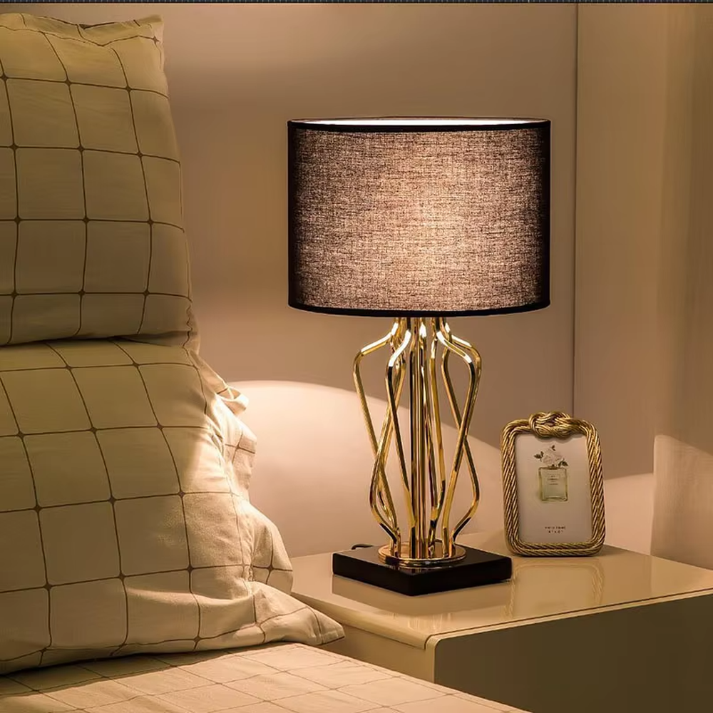Modern luxurious black-gold geometric interwoven metal stand table lamp (black fabric lampshade + golden interwoven poles + black base), warm light effect, creating a high-end artistic atmosphere.