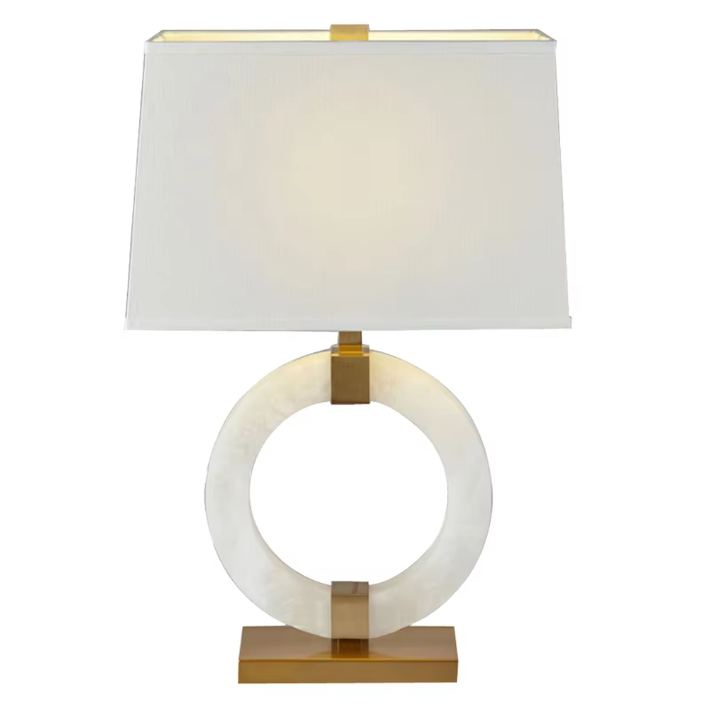 Modern light luxury style table lamp with a white natural stone/acrylic ring paired with gold metal brackets and base, and a rectangular white fabric lampshade. It emits soft and even light, combining decorativeness and practicality, suitable for lighting and decoration in spaces such as bedroom nightstands, living room side tables, and hotel guest rooms.