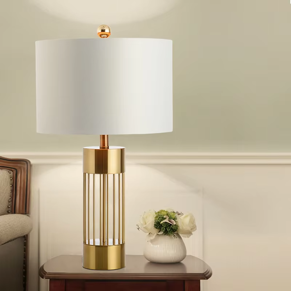 This light luxury table lamp features a gold metal hollow vertical strip column base, paired with a white fabric cylindrical lampshade and a top gold spherical decoration, with a simple and elegant shape, serving both lighting and decorative purposes, ideal for bedroom bedside tables, living room side tables, light luxury homestays and other spaces.