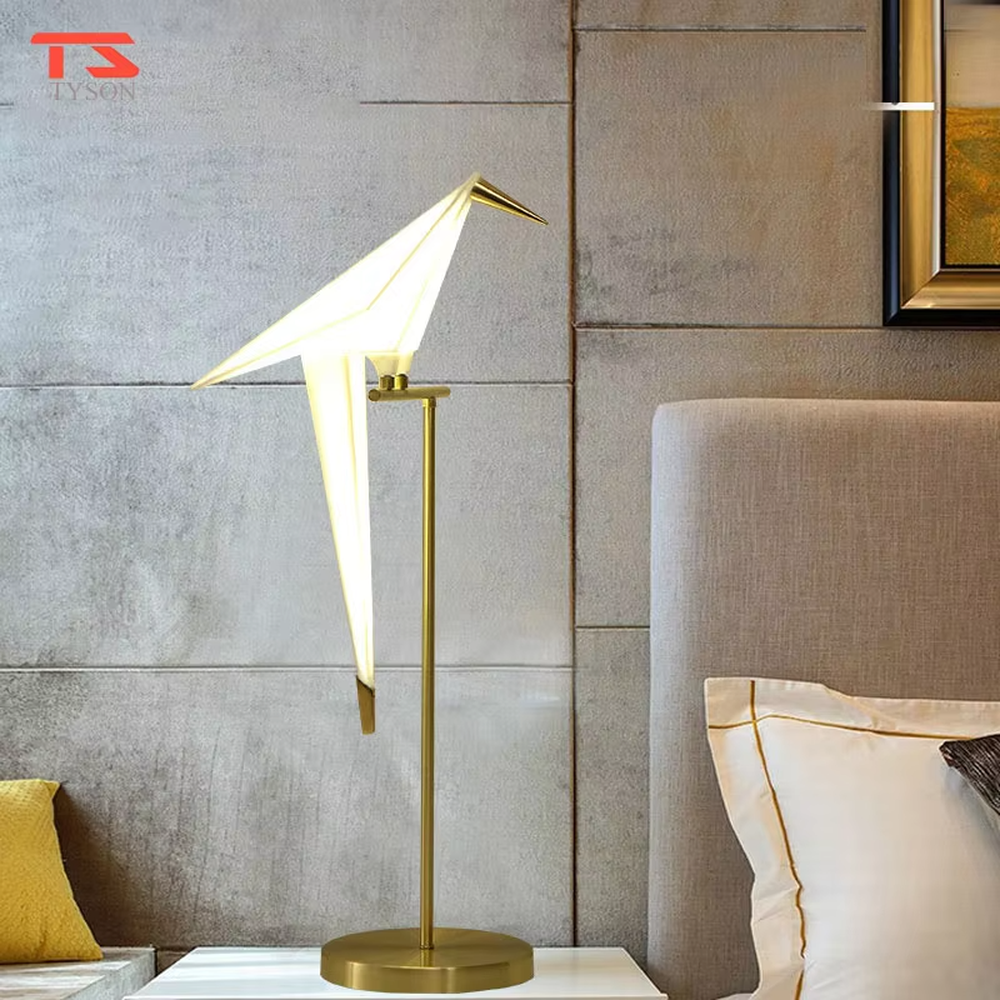 This is a modern light luxury origami crane-shaped table lamp, featuring a gold metal stand paired with a translucent paper art lamp body. The lamp body is as dynamic and soft as an origami crane, serving both lighting and artistic decoration purposes, suitable for bedroom nightstands, light luxury living room side tables, hotel guest rooms, showrooms and other scenarios.