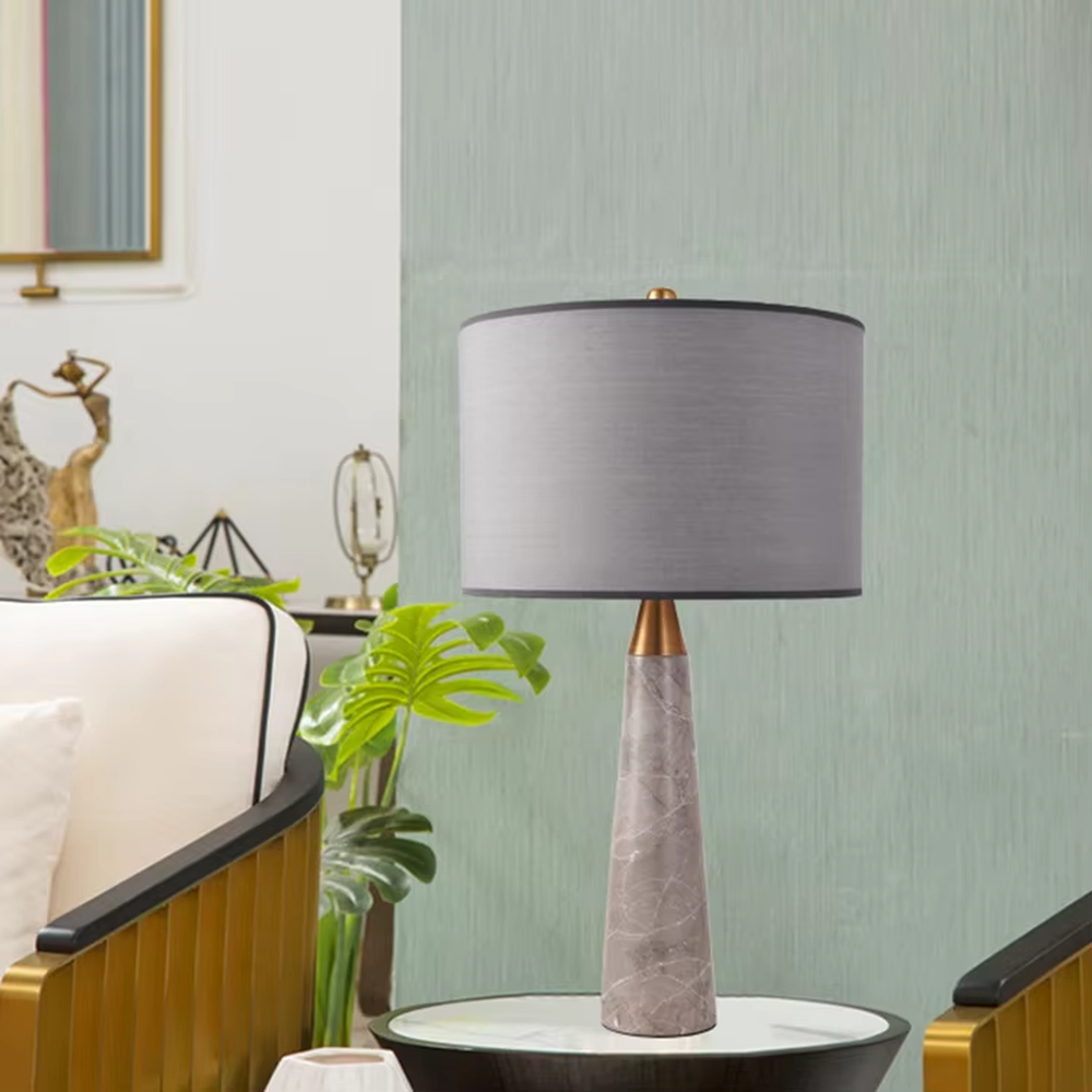 Light luxury marble cone table lamp, with a grey natural marble base, gold metal connection, off-white fabric lampshade with black trim, providing soft and warm light, designed to enhance the delicate texture of spaces, suitable for bedroom nightstands, living room side tables, modern light luxury homes and hotel guest rooms, etc.