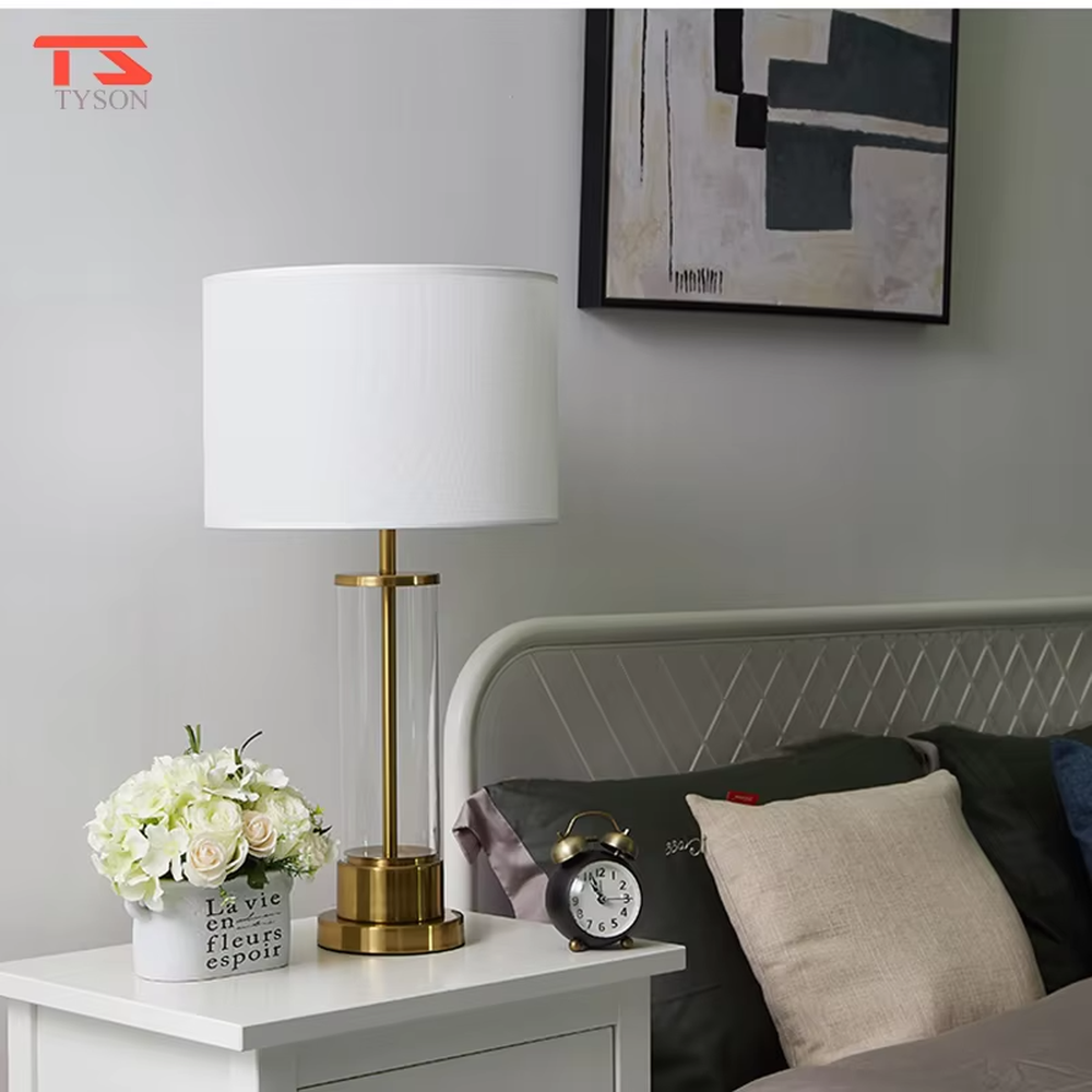 This modern light luxury table lamp features a transparent glass lamp body, paired with gold metal connectors and base, and an off-white fabric cylindrical lampshade that transmits light softly. It serves both lighting and decorative purposes, ideal for light luxury spaces such as bedroom bedside tables, living room side tables, and hotel guest rooms.