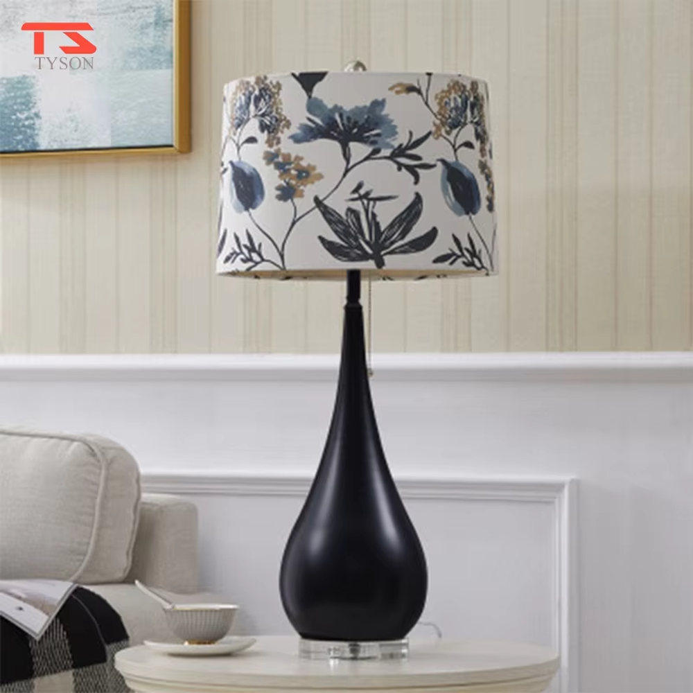This is a pastoral-style floral fabric table lamp, with an off-white lampshade printed with blue and black floral patterns, paired with a black matte teardrop-shaped base and transparent crystal feet, featuring both decorative and lighting functions, ideal for warm indoor scenarios such as bedroom nightstands and living room side tables.