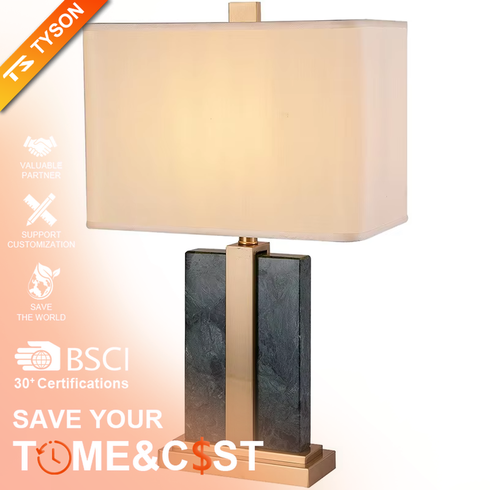 Modern light luxury marble and metal spliced table lamp, with a gray marble lamp body paired with gold metal decorative strips, a light gray fabric rectangular lampshade (with a gold ball decoration on top), emitting soft and elegant light, combining decorativeness and practicality, suitable for lighting and decoration in spaces such as bedroom nightstands, living room side tables, and hotel guest rooms.