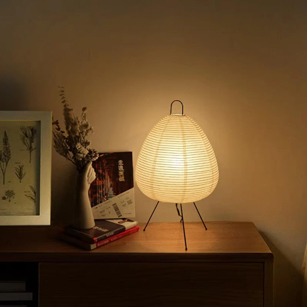 This wabi-sabi style egg-shaped table lamp features a striped light-transmitting paper lampshade, supported by a black metal tripod, with a simple and soft shape, serving both lighting and decorative purposes, ideal for bedroom bedside tables, homestay rooms, wabi-sabi style spaces and other scenarios.
